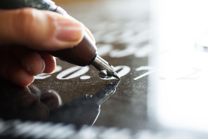 Hand holding a pen engraving the numbers 