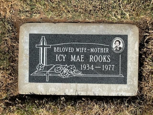 Gravestone of Icy Mae Rooks, 1934-1977. Black granite, with a cross, portrait, and floral design, set in a concrete border.