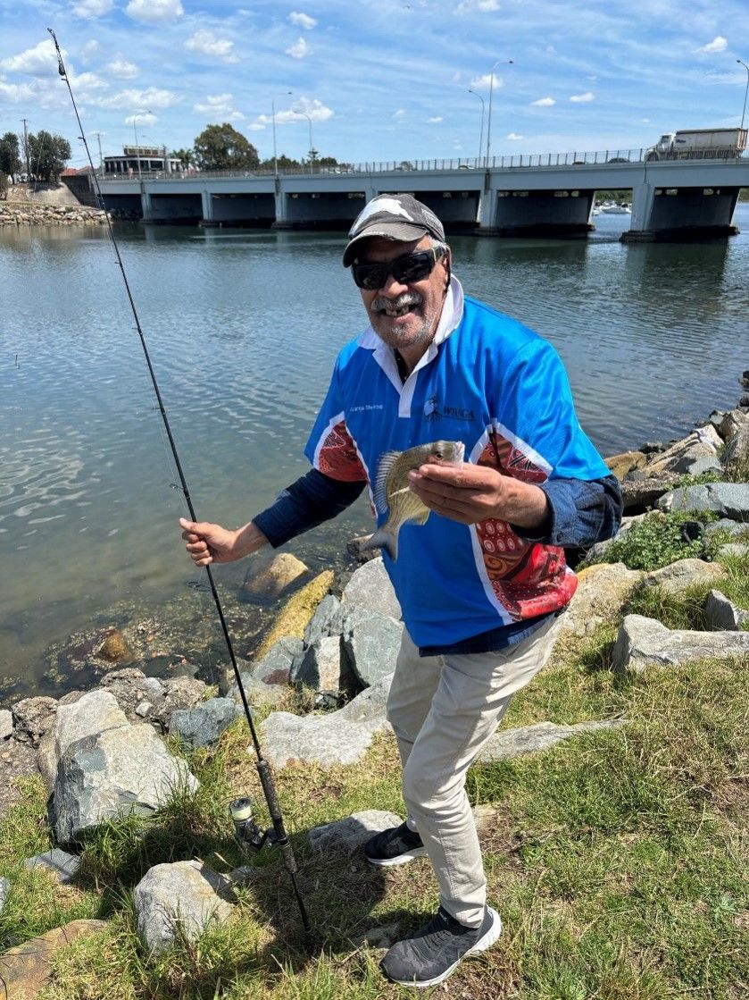 A man is standing next to a river holding a fishing rod and a fish.