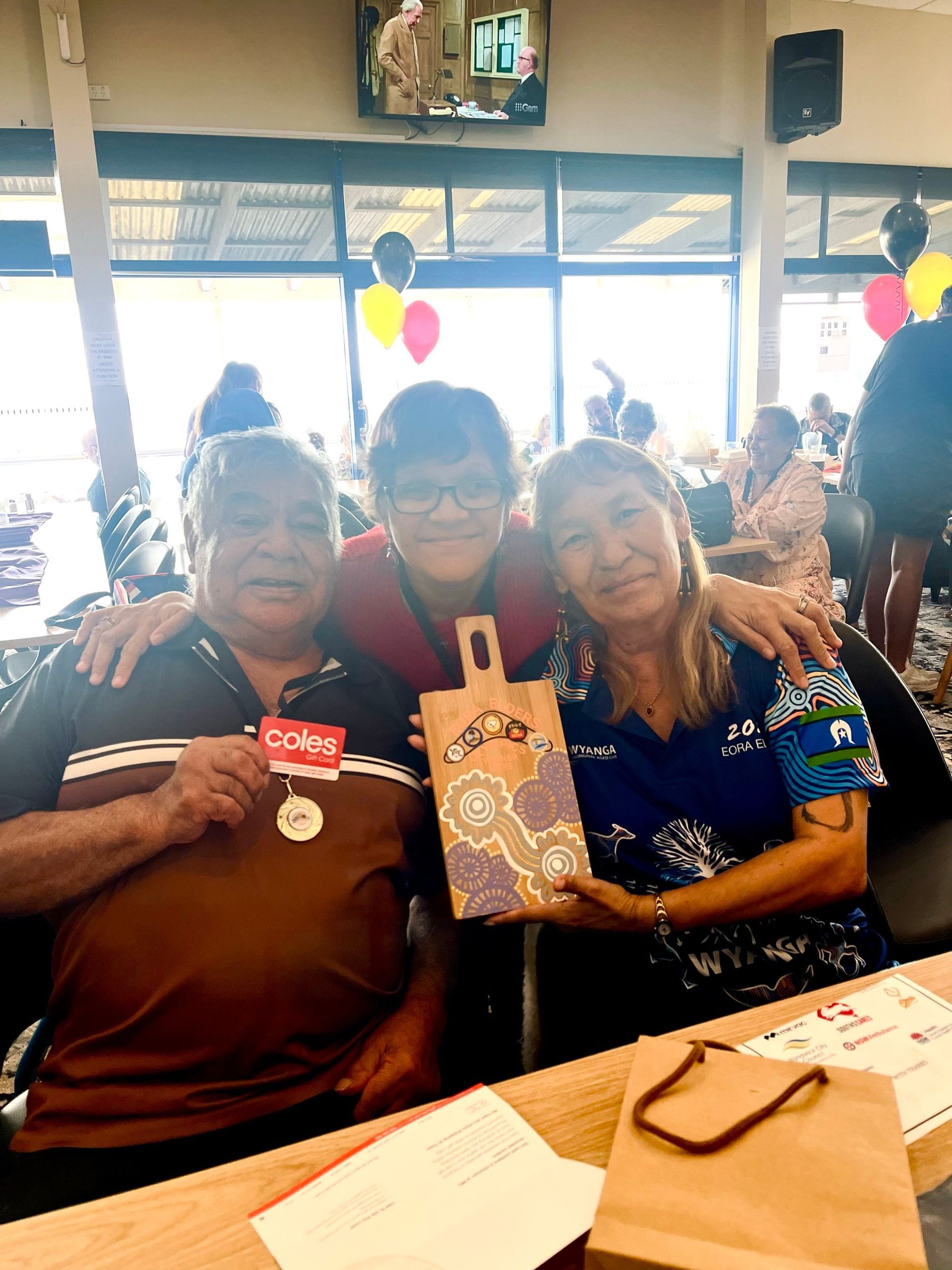 Three women are sitting at a table holding a gift bag.