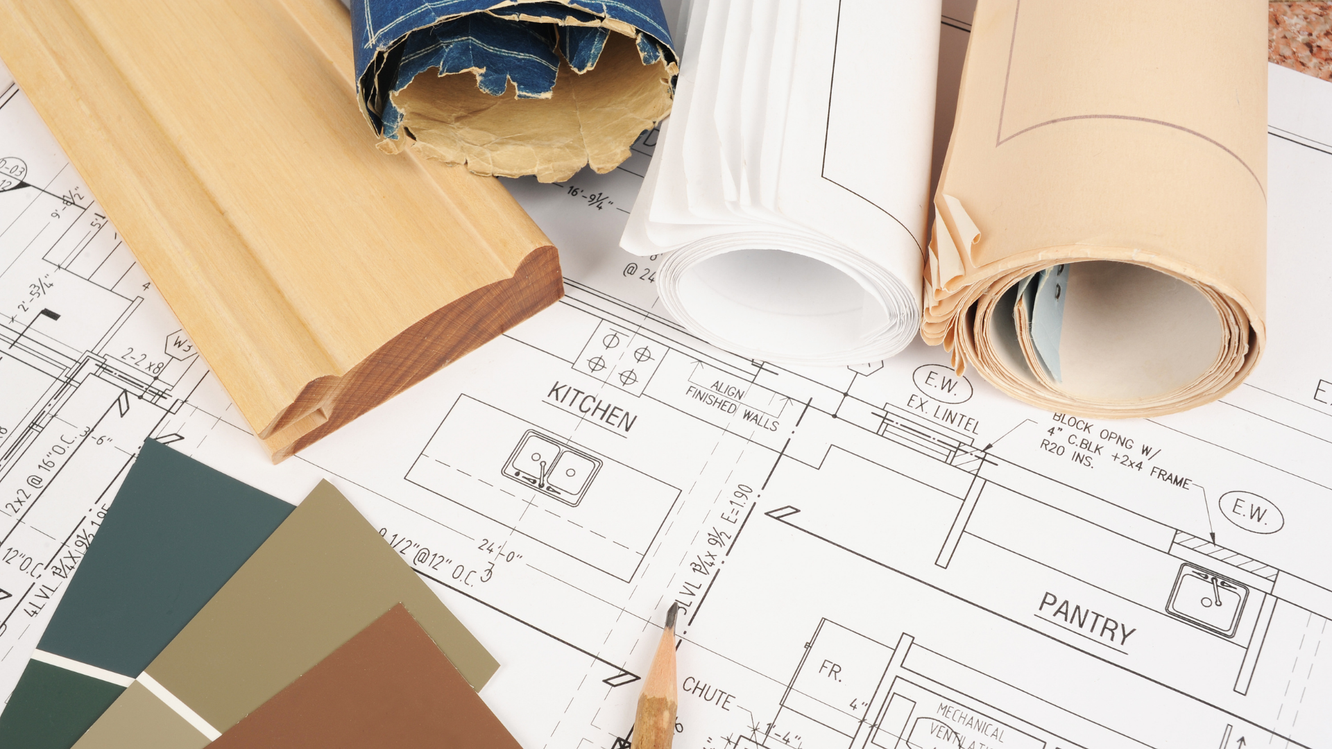 Architectural blueprints, paint swatches, and rolled plans with a wooden molding piece.