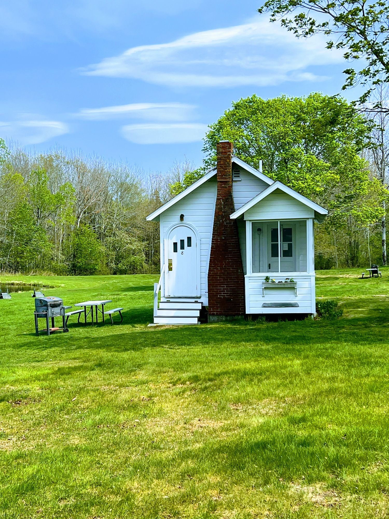 A small white house with a chimney is sitting in the middle of a lush green field.