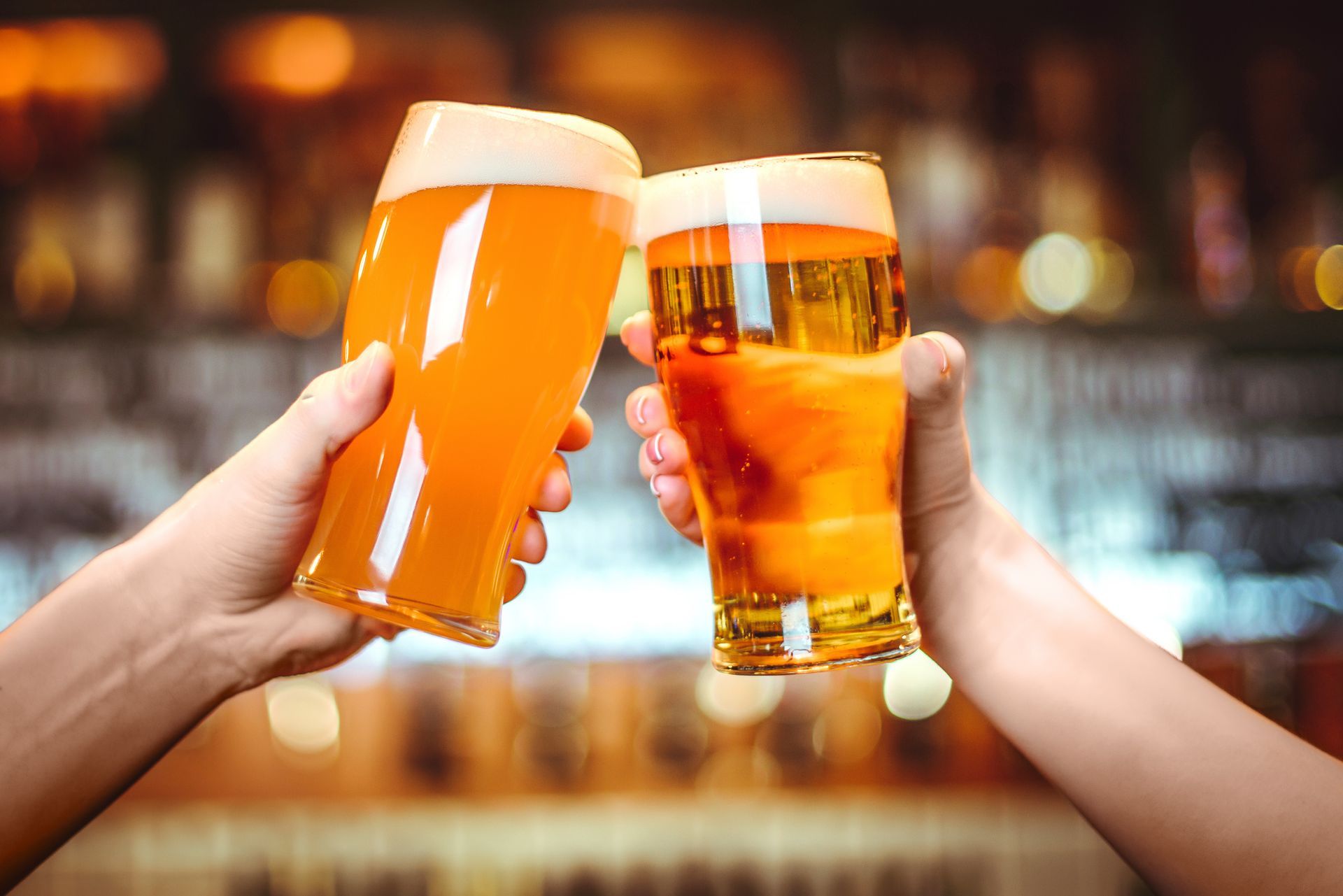 Two people are toasting with two glasses of beer in a bar.