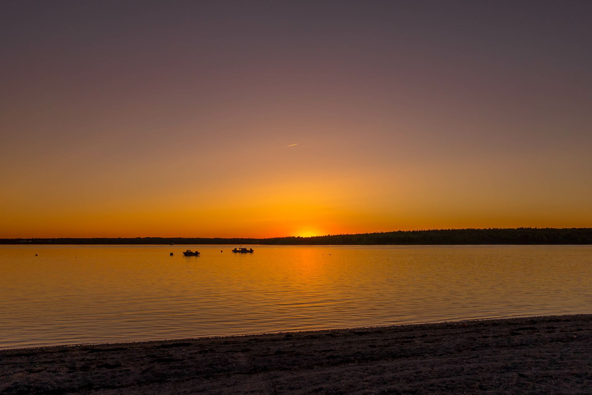 A sunset over a body of water with boats in the distance.