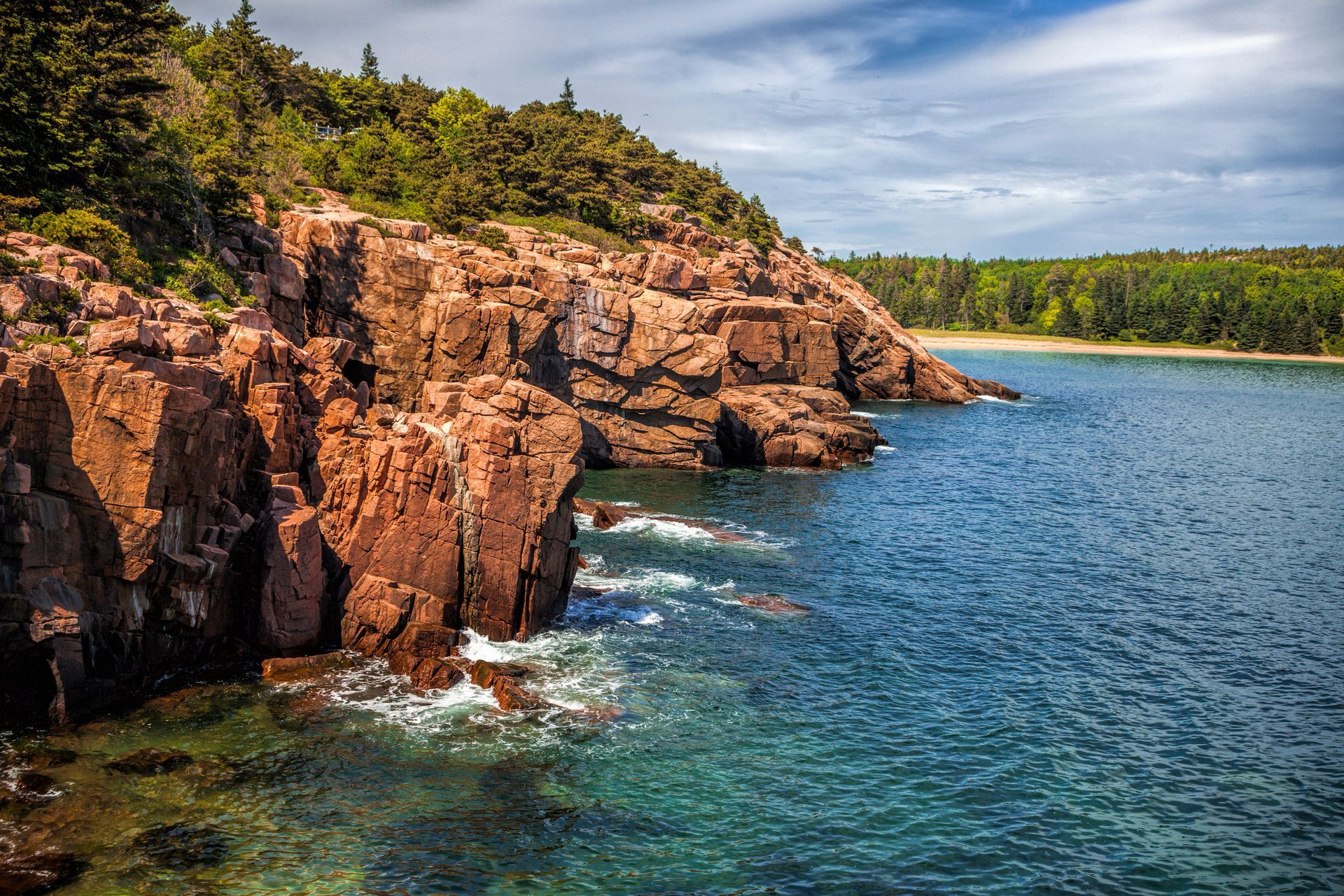 A cliff overlooking a body of water with trees on the shore.