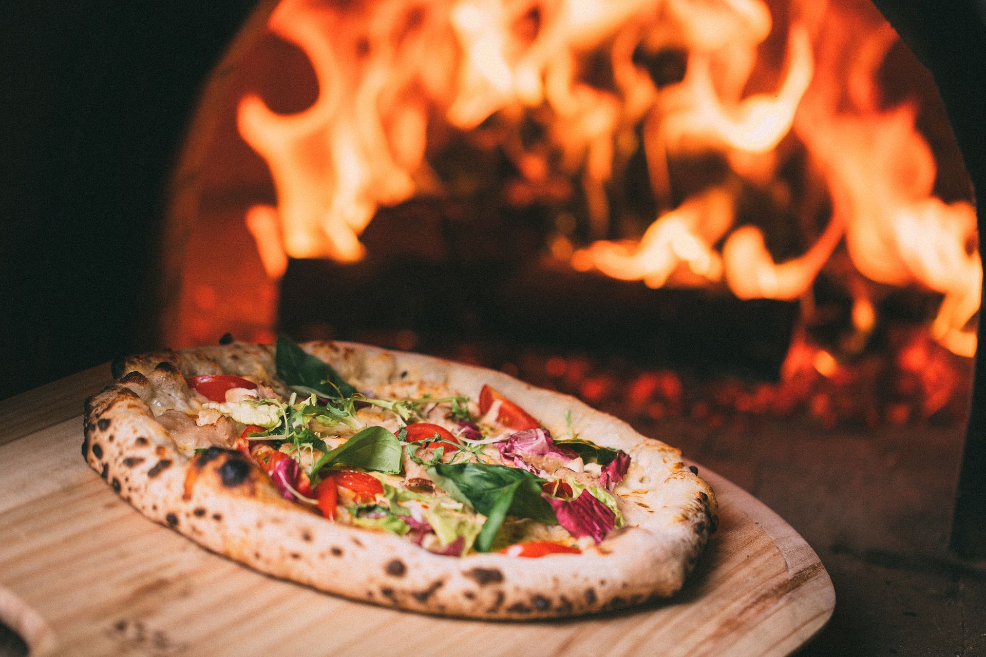 A pizza is sitting on a wooden cutting board in front of an oven.