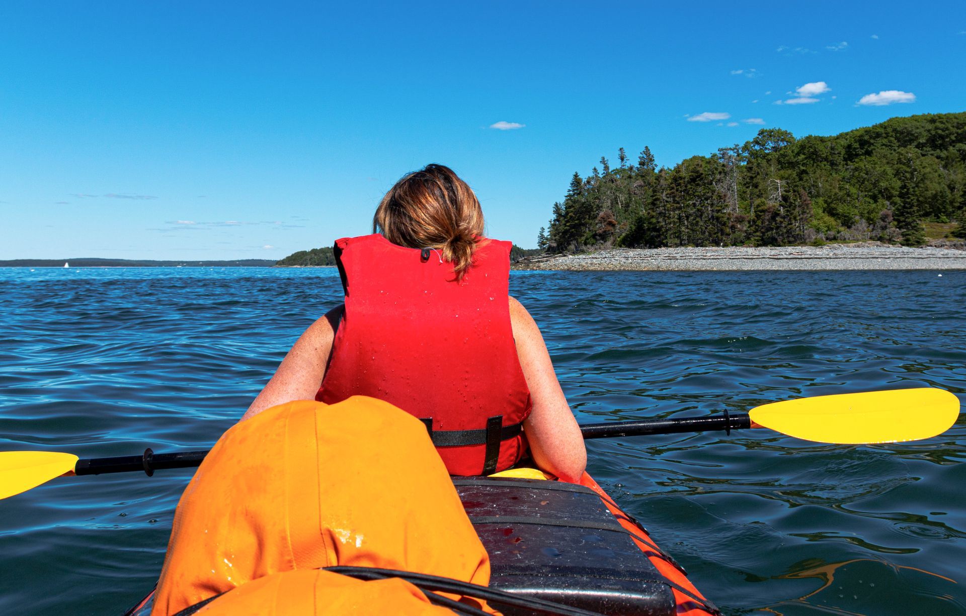 A woman in a life jacket is paddling a kayak on a lake.