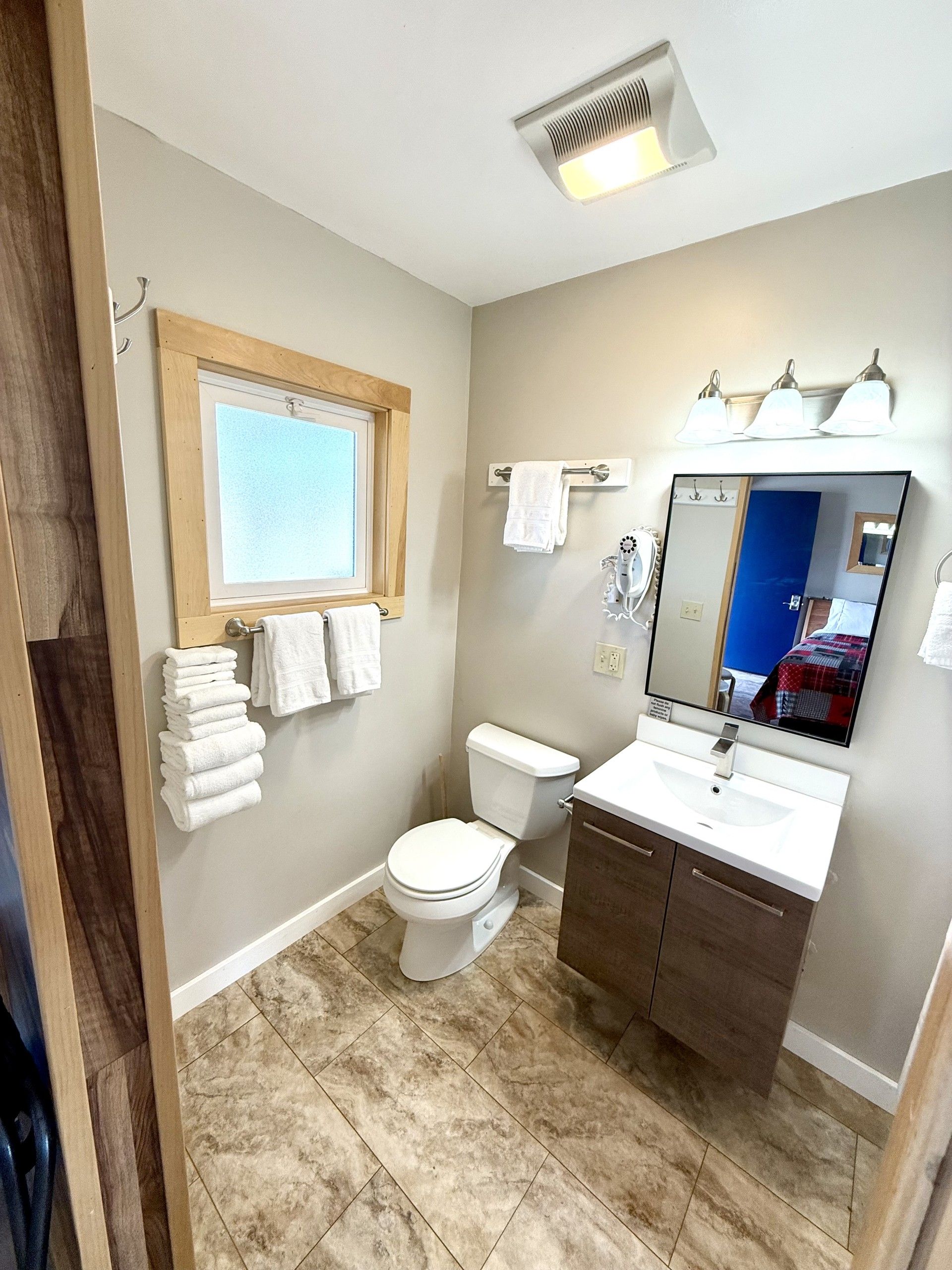 A bathroom with a toilet , sink , mirror and window.