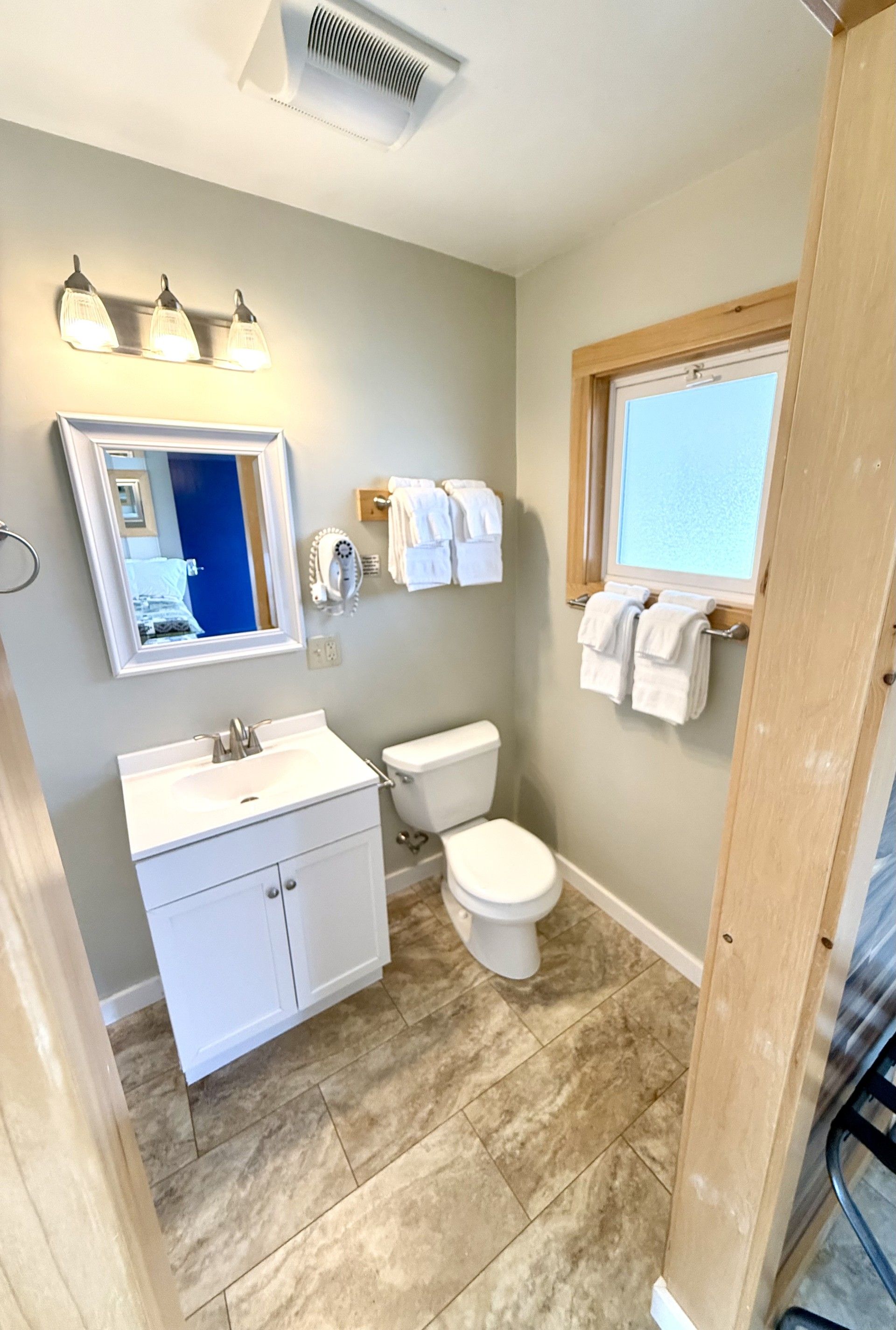 A bathroom with a toilet , sink , mirror and window.