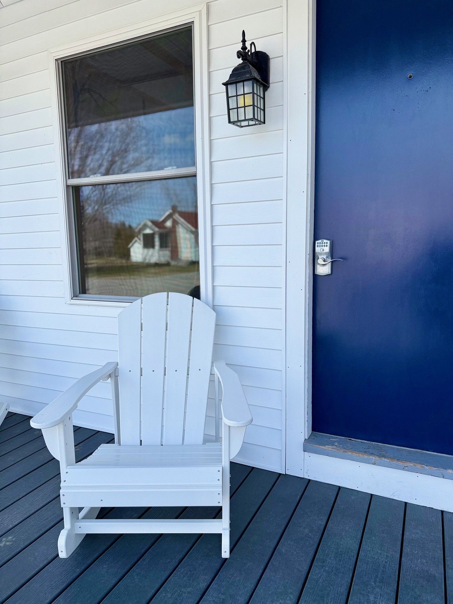 A white adirondack chair is sitting on a porch in front of a blue door.