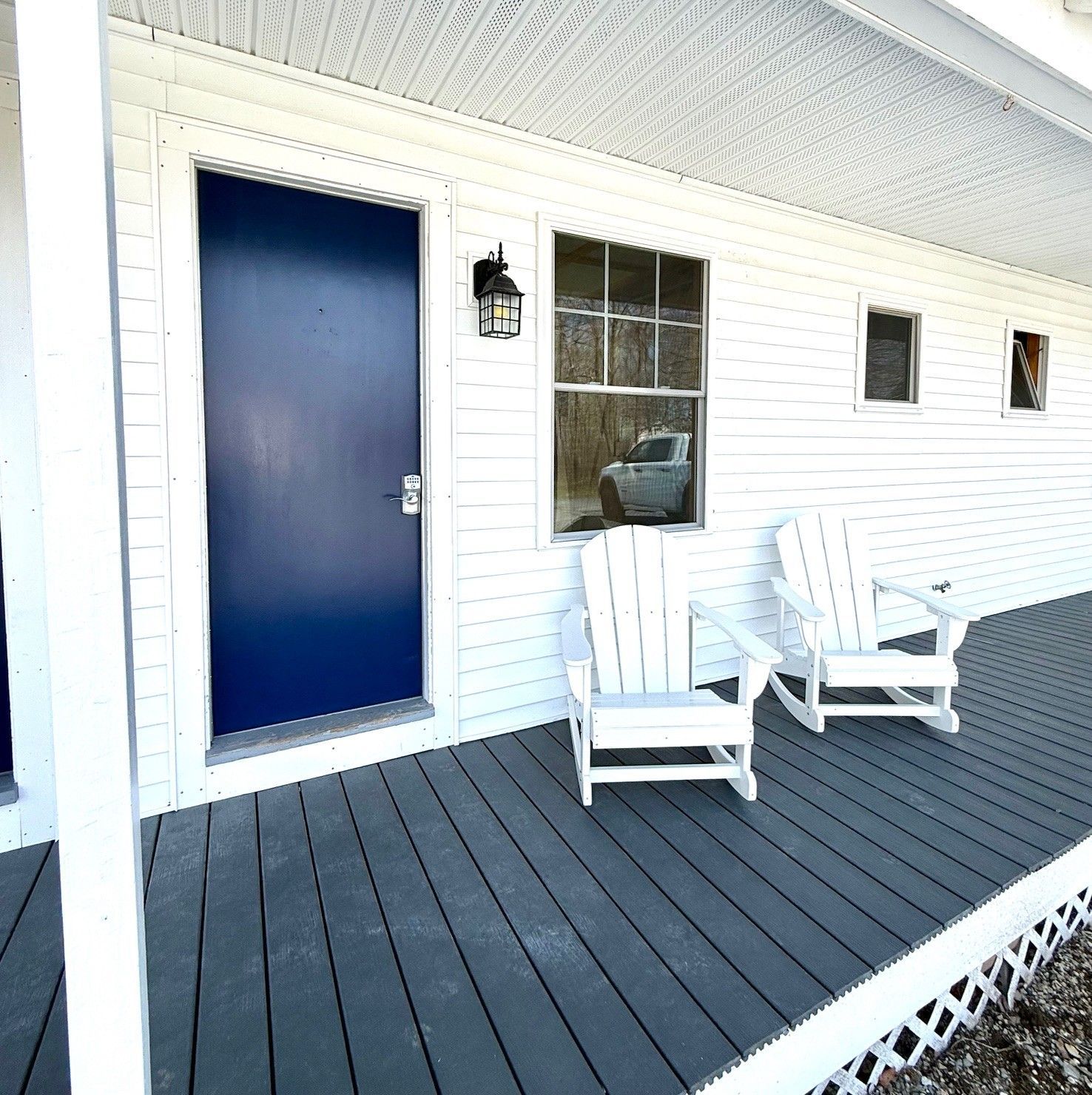 A white house with a blue door and two chairs on the porch
