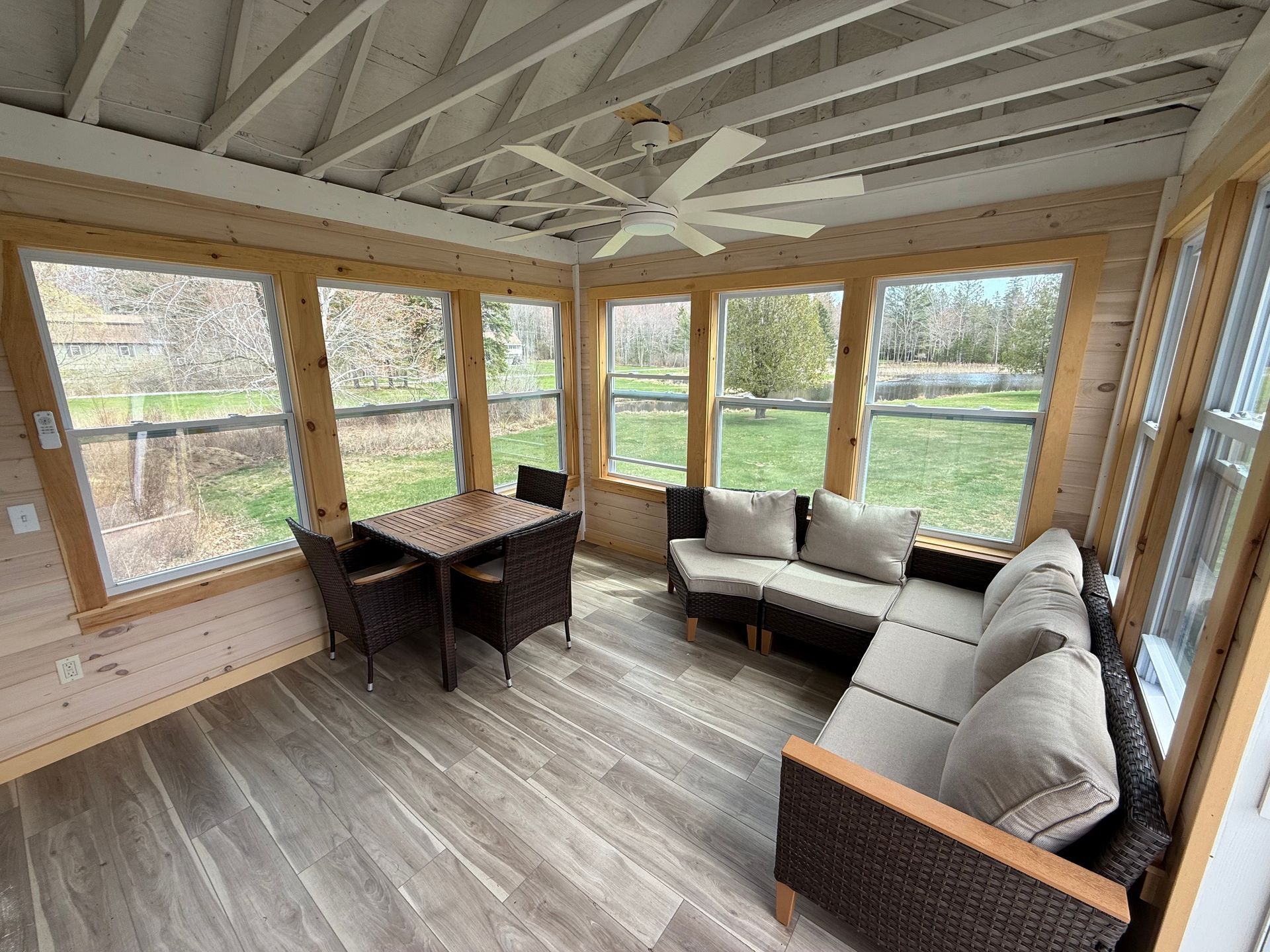 A screened in porch with a couch , table and chairs.