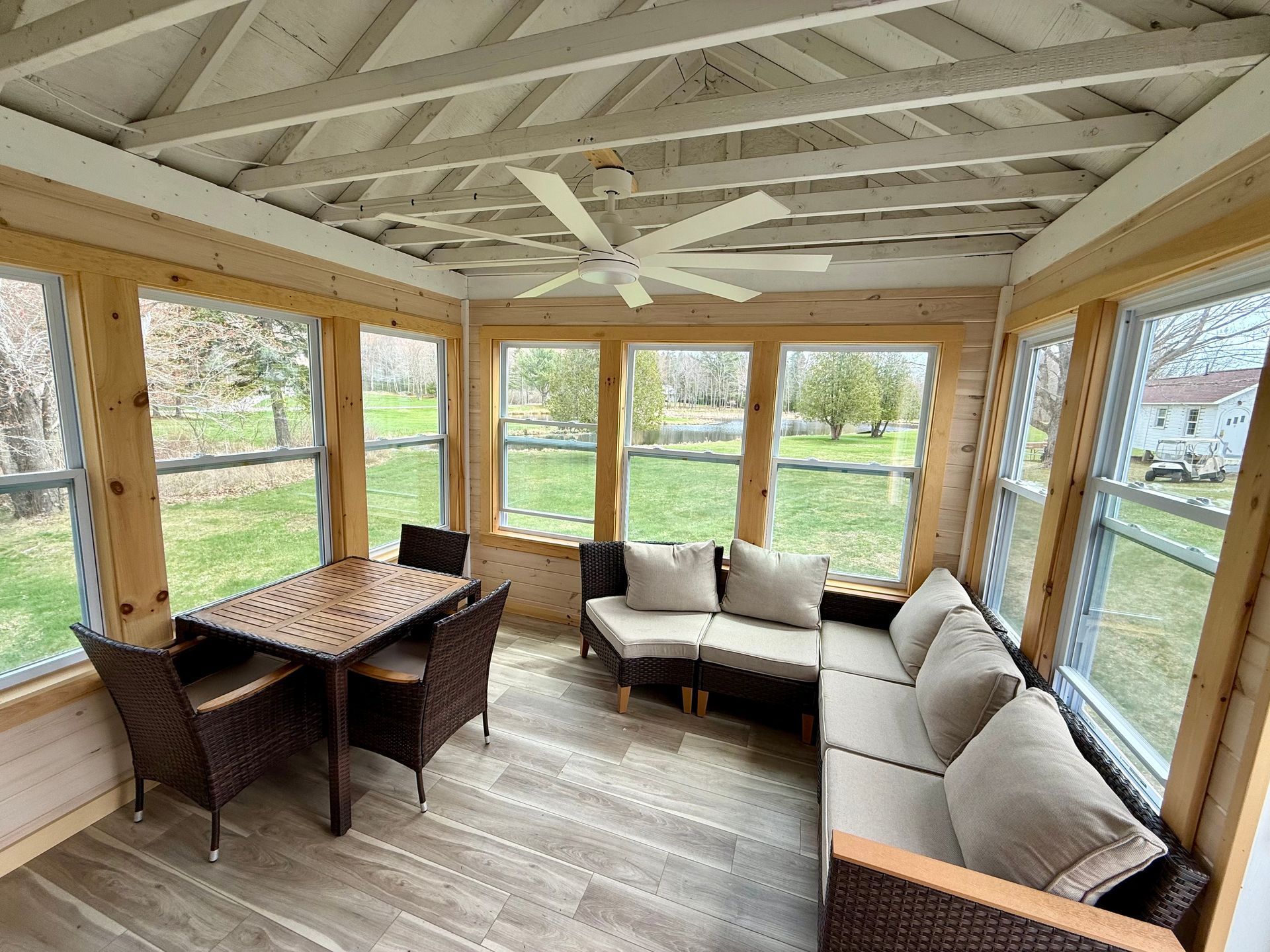 A screened in porch with a couch , chairs , table and ceiling fan.