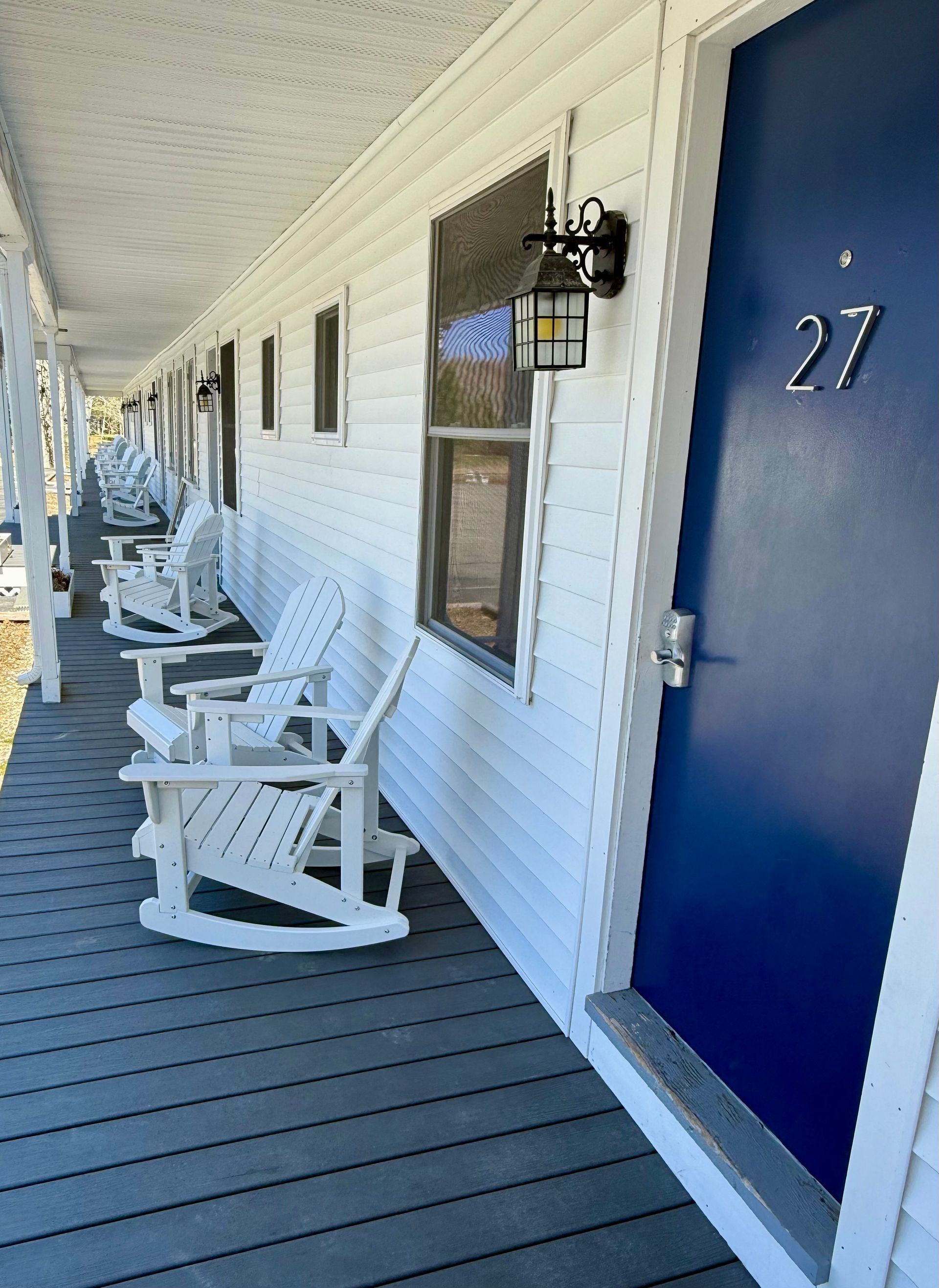 A row of white rocking chairs on a porch next to a blue door.