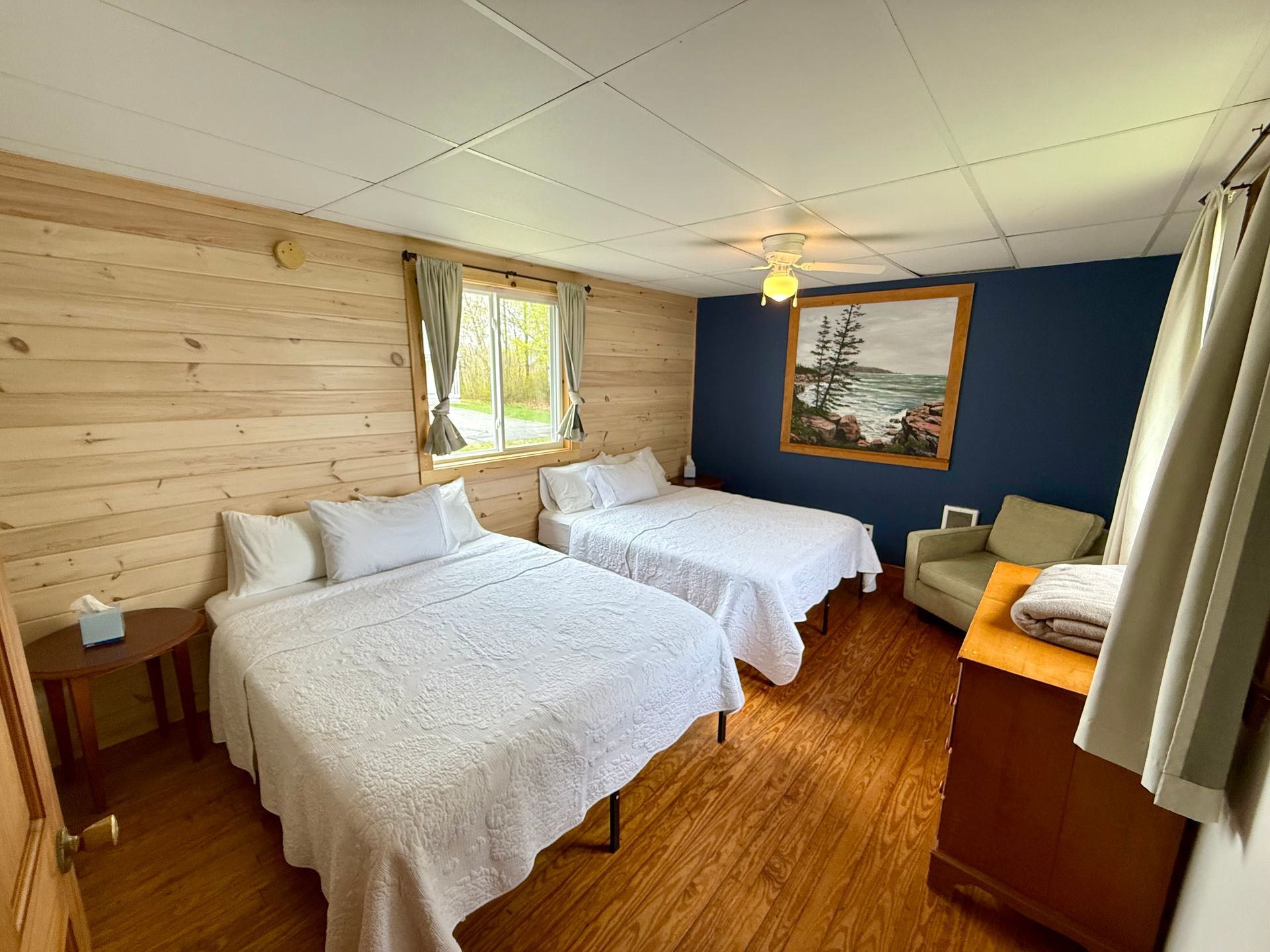 A bedroom with two beds , a chair and a dresser.