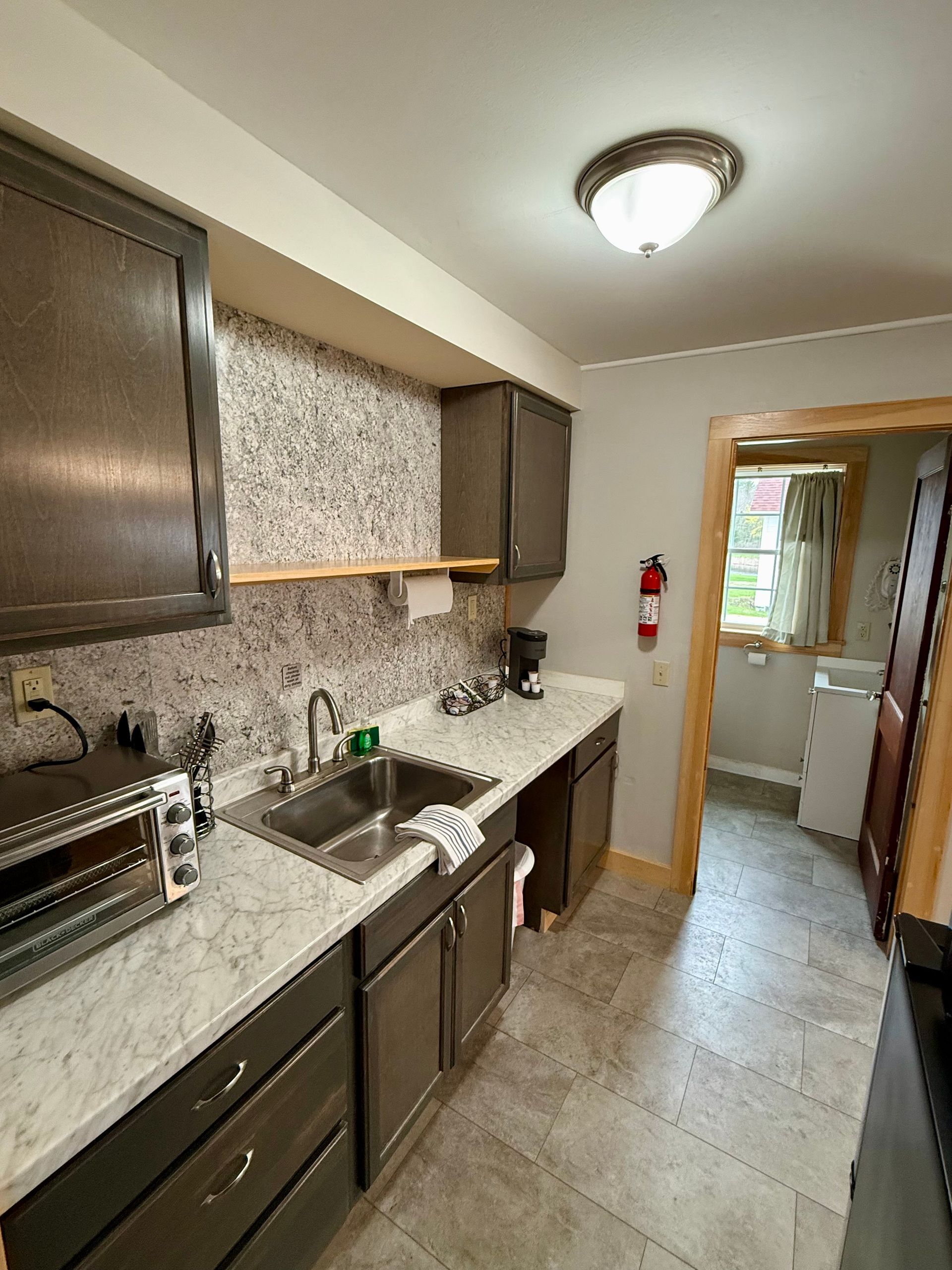 A kitchen with a sink , cabinets , a microwave , and a fire extinguisher.