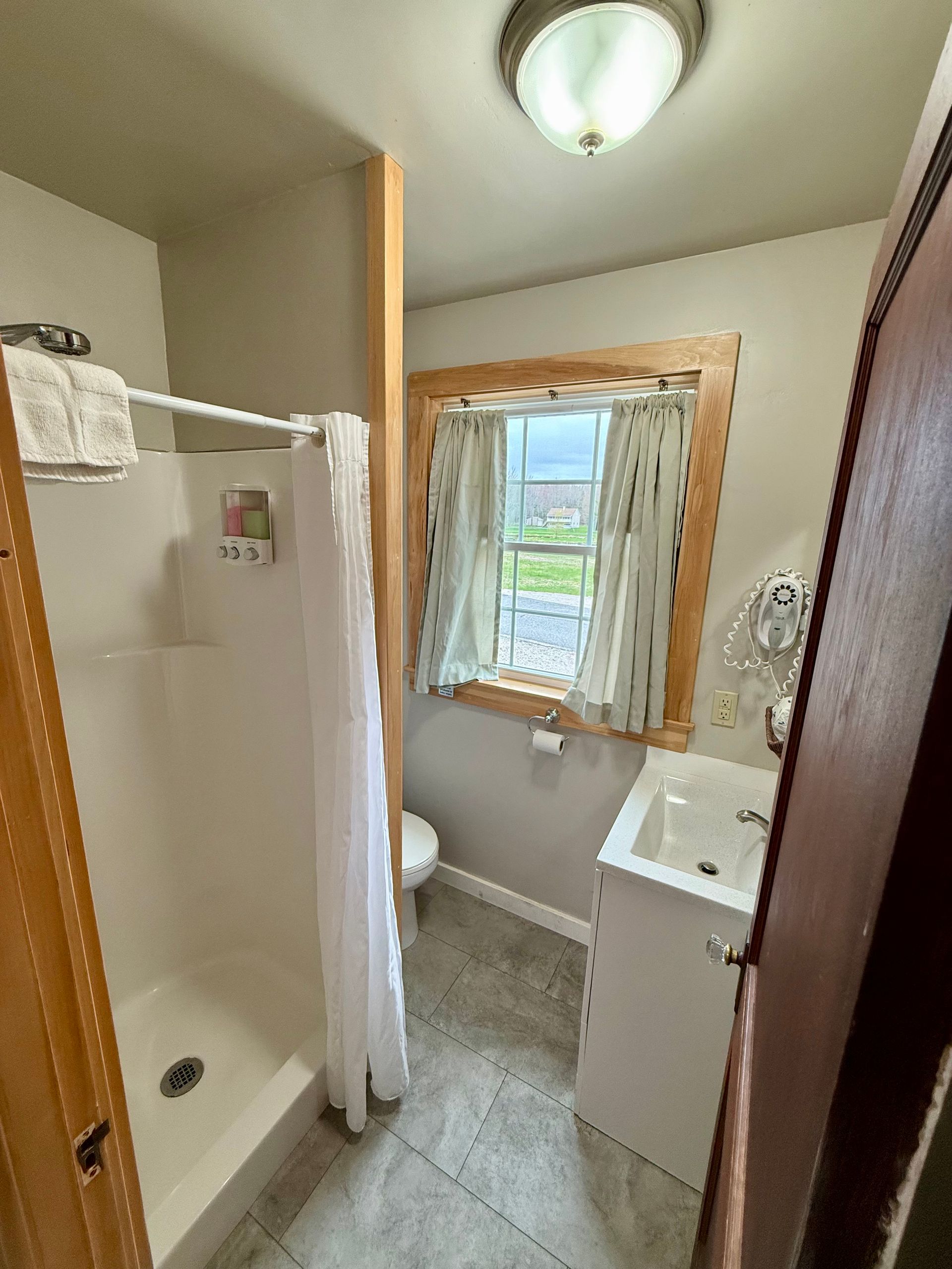 A bathroom with a shower , sink , toilet and window.