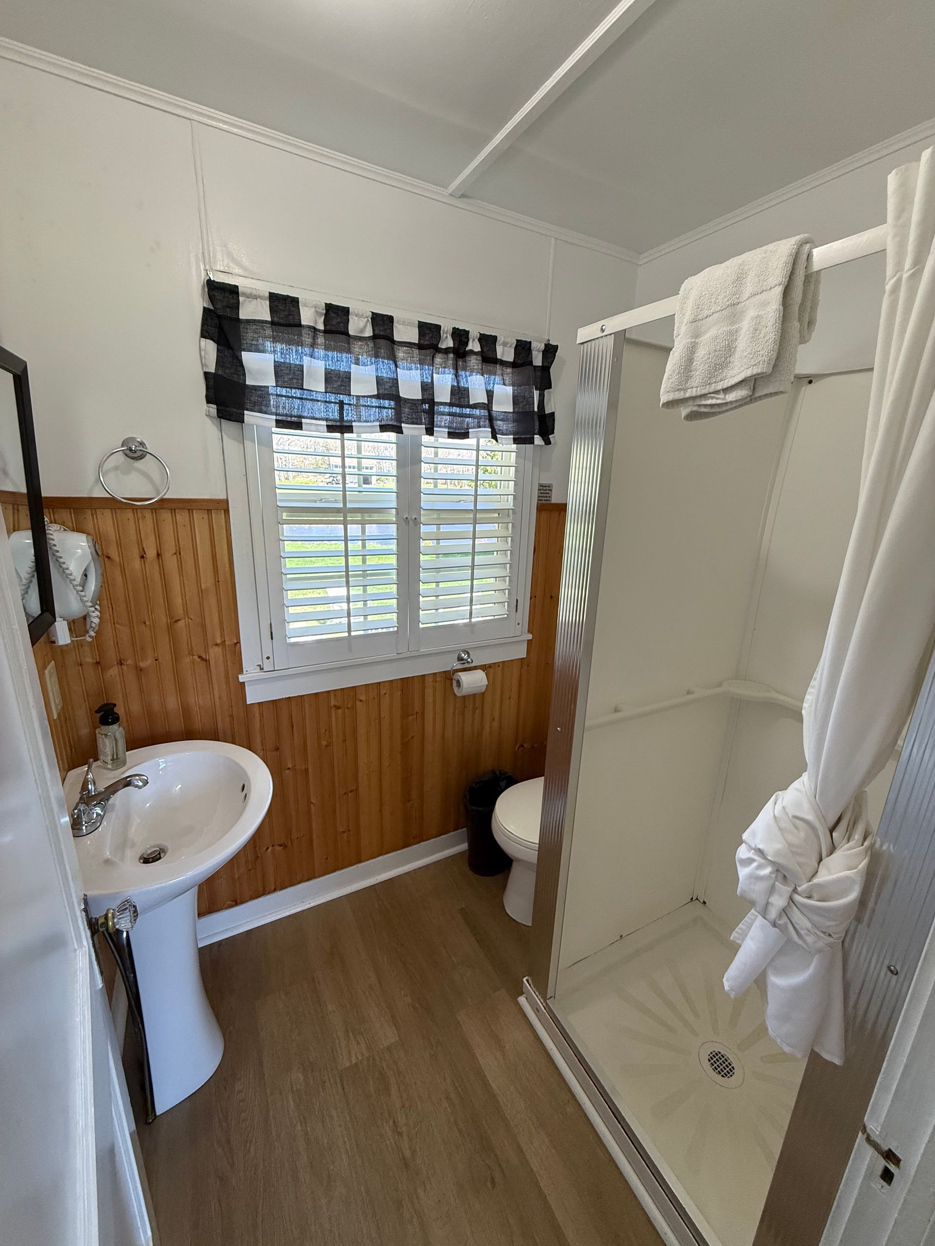 A bathroom with a sink , toilet , shower and window.