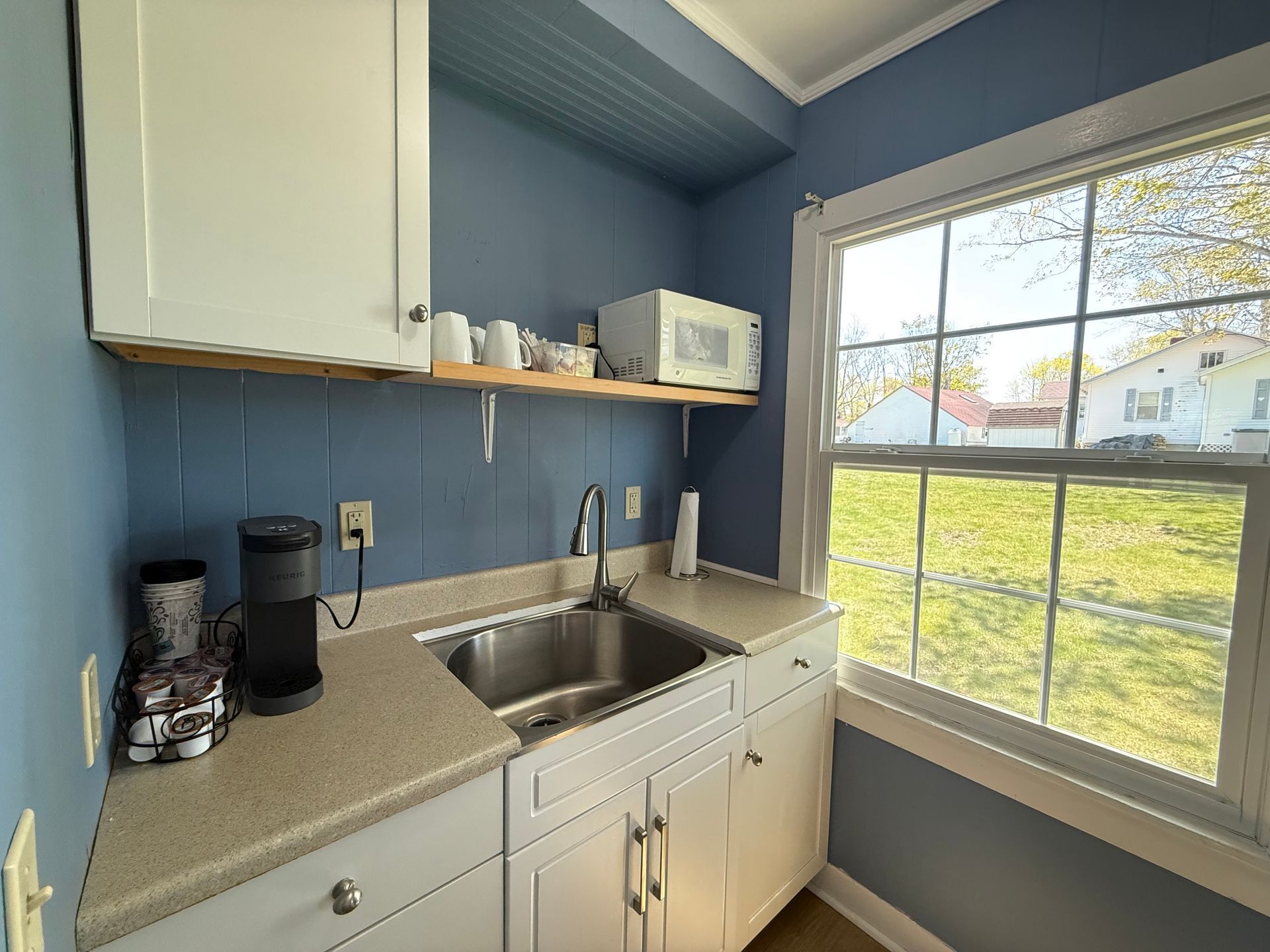 A kitchen with a sink , microwave , coffee maker and a window.