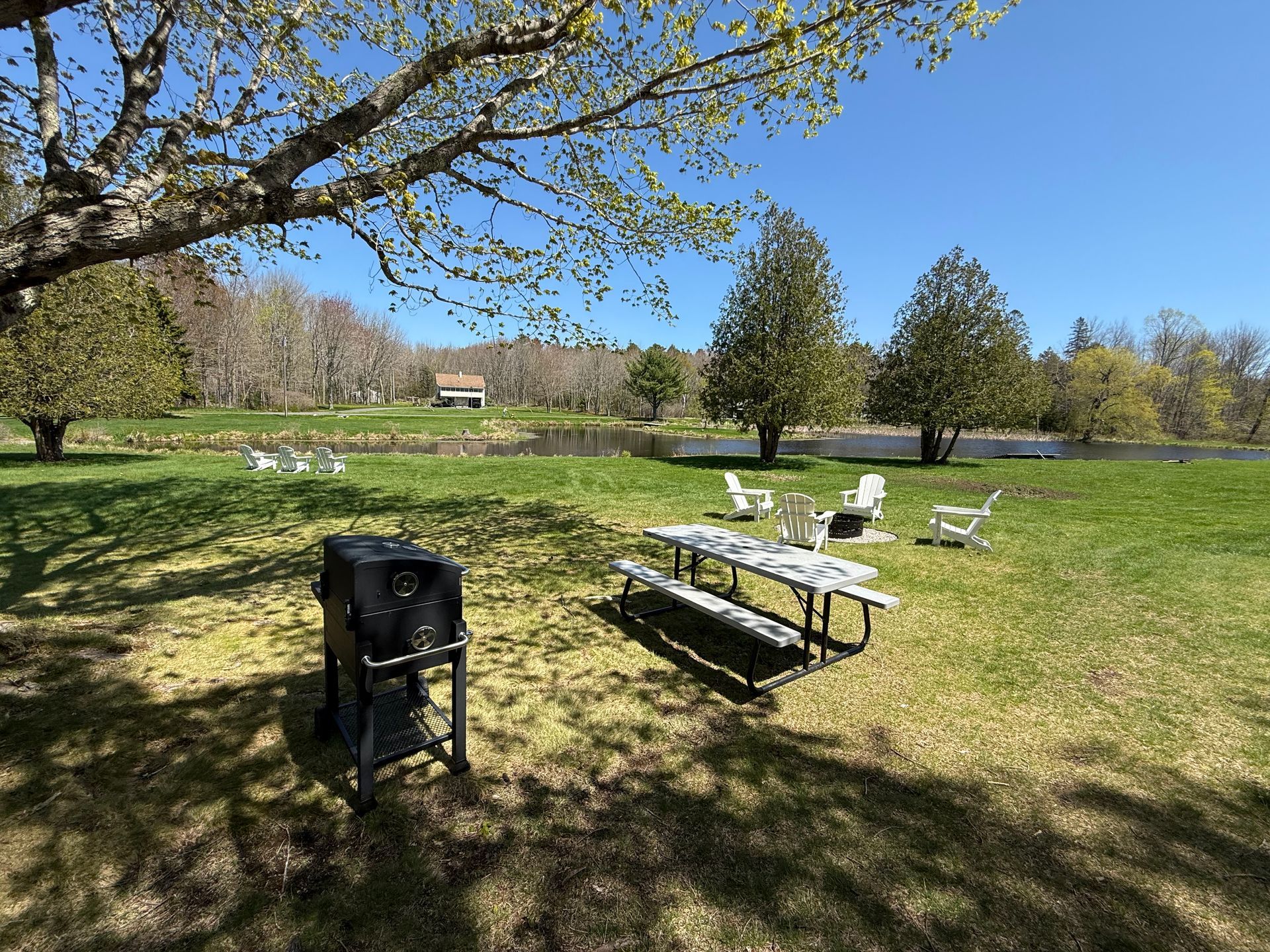 A picnic table and grill in a park with a lake in the background.