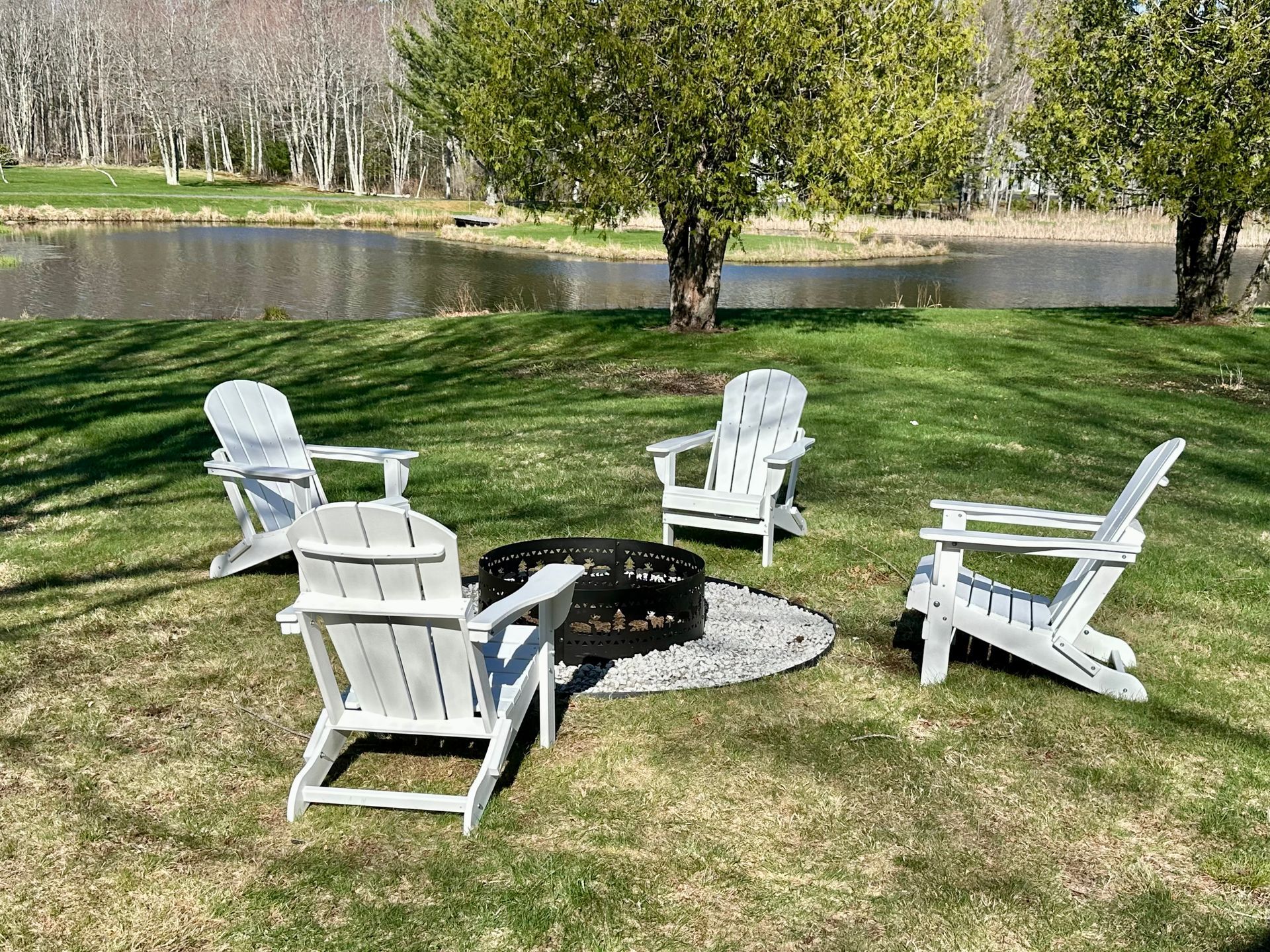 A group of white chairs are sitting around a fire pit in the grass.