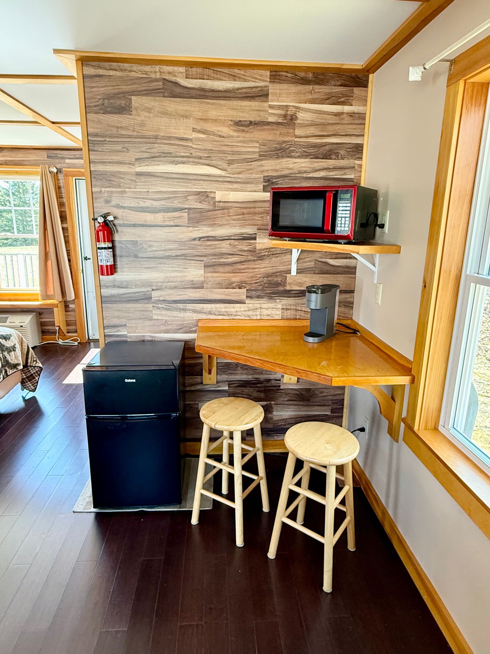 A room with a table , stools , a microwave and a refrigerator