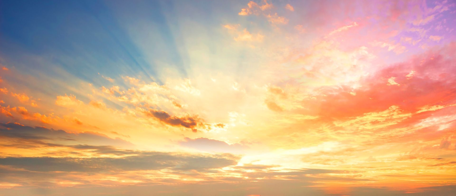 Vibrant sky with blue, orange, and pink hues; sun rays breaking through clouds.