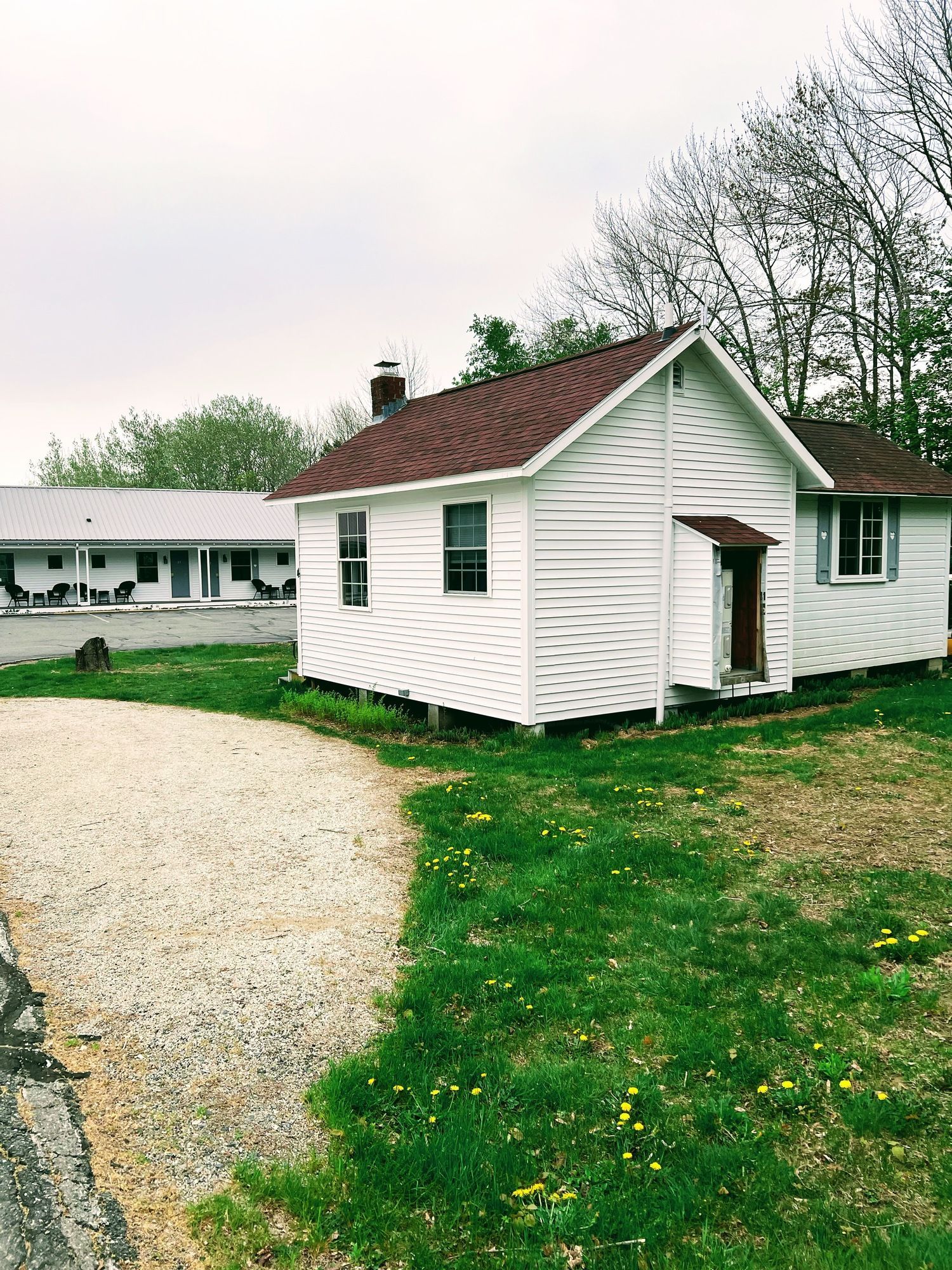 A small white house with a red roof is sitting in the middle of a grassy field.