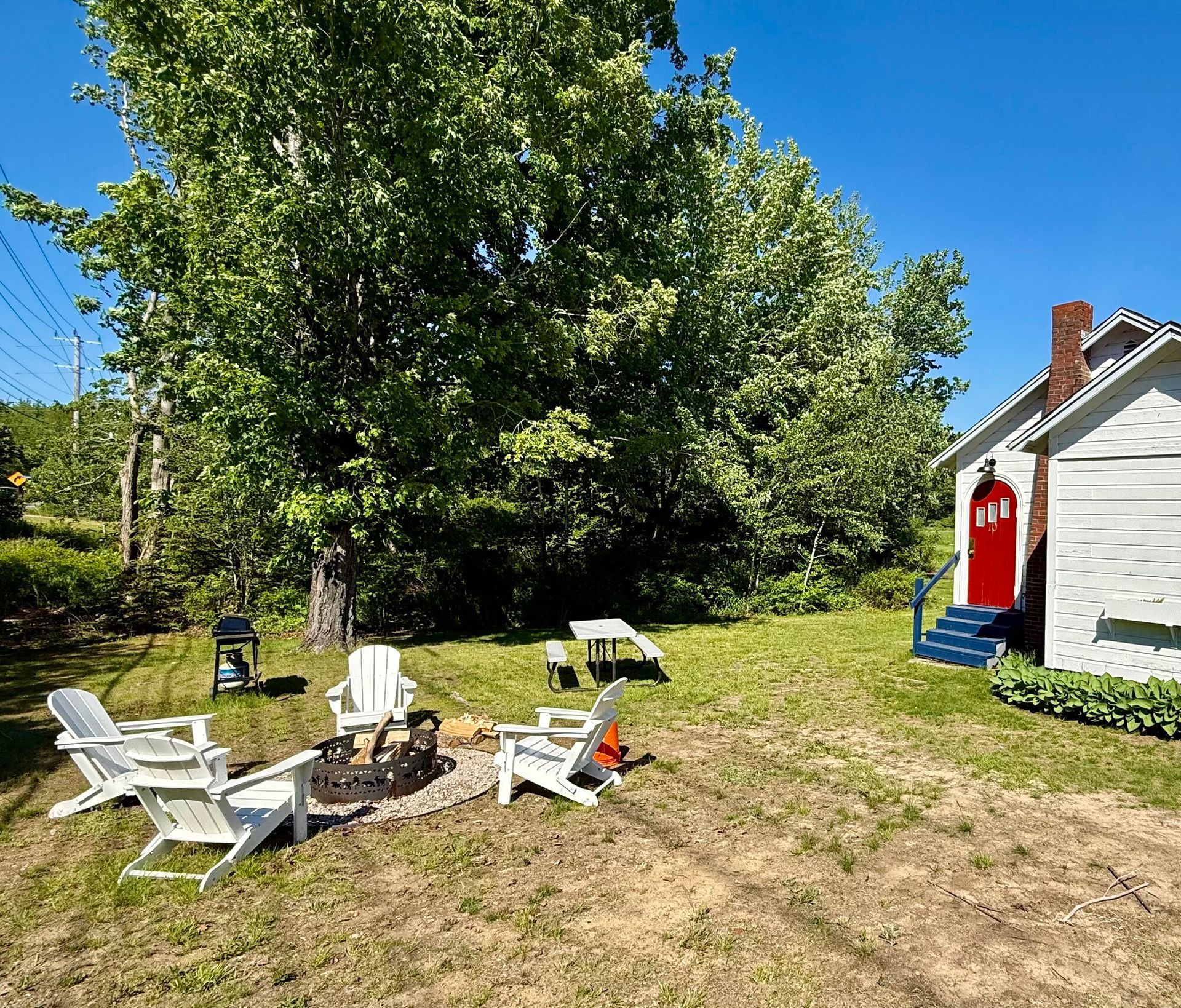 Weathered white house with red roof, small porch, and yard, surrounded by trees.