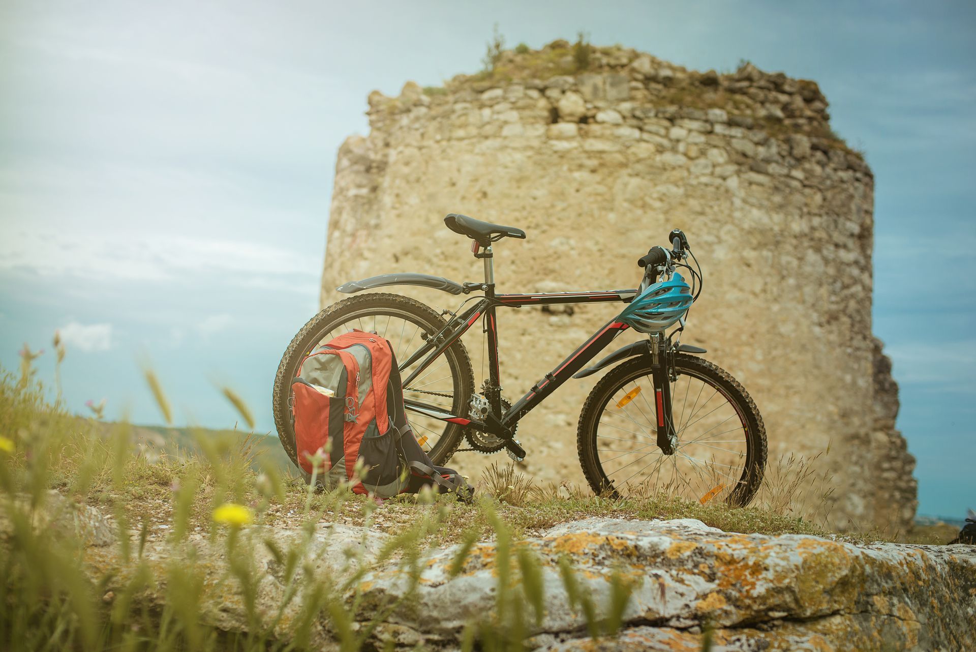 Black mountain bike with red backpack sits on a stone wall in front of a weathered stone tower.