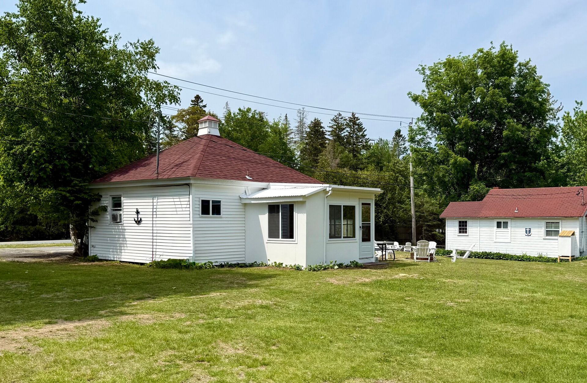 White house with red roof and small outbuilding on a grassy lawn surrounded by trees