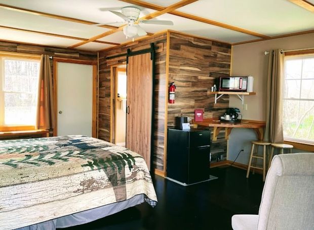 A bedroom with a sliding barn door , a bed , a chair , a microwave and a refrigerator.