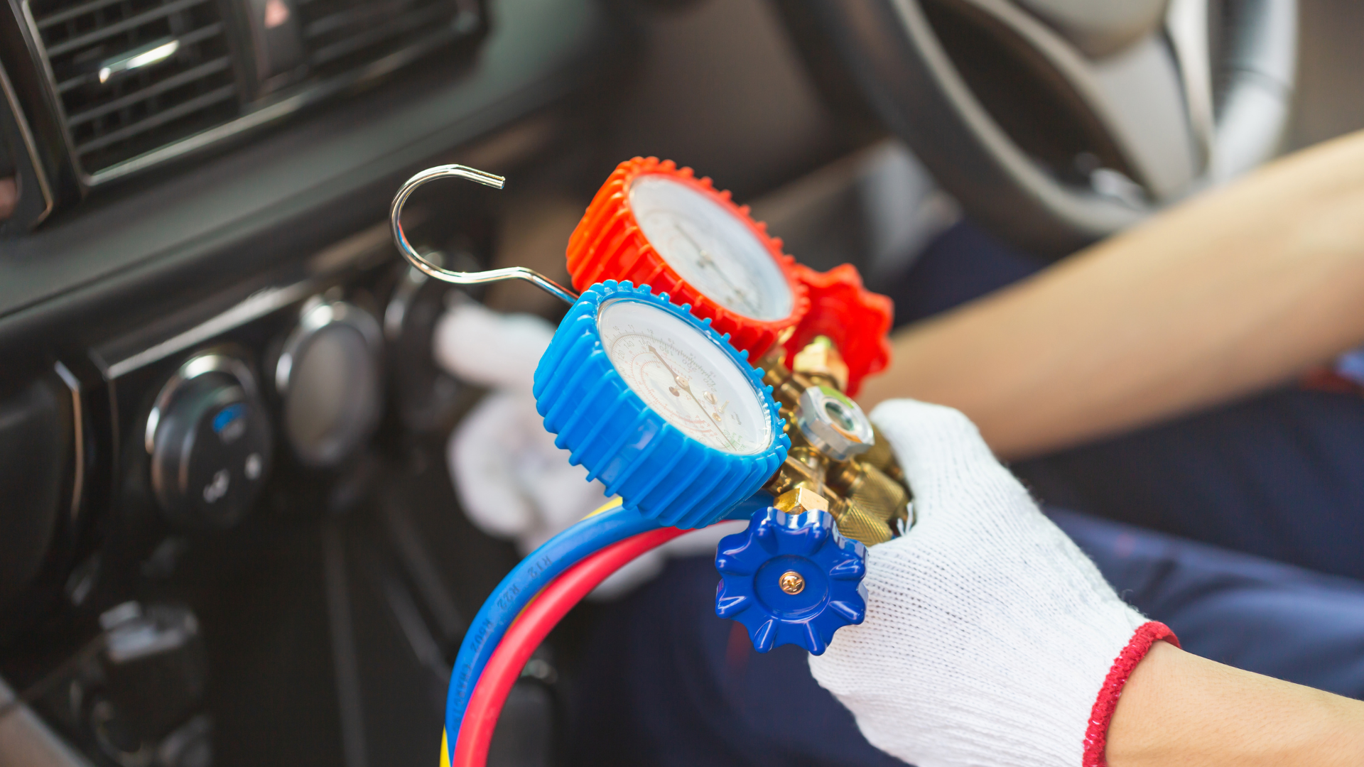 Person in white gloves using gauges to check car AC system. Gauges have red and blue dials.
