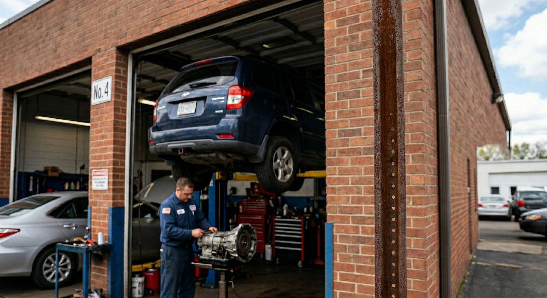 A technician works on a car component in a brick automotive repair shop where a dark SUV is lifted on a hydraulic lift.