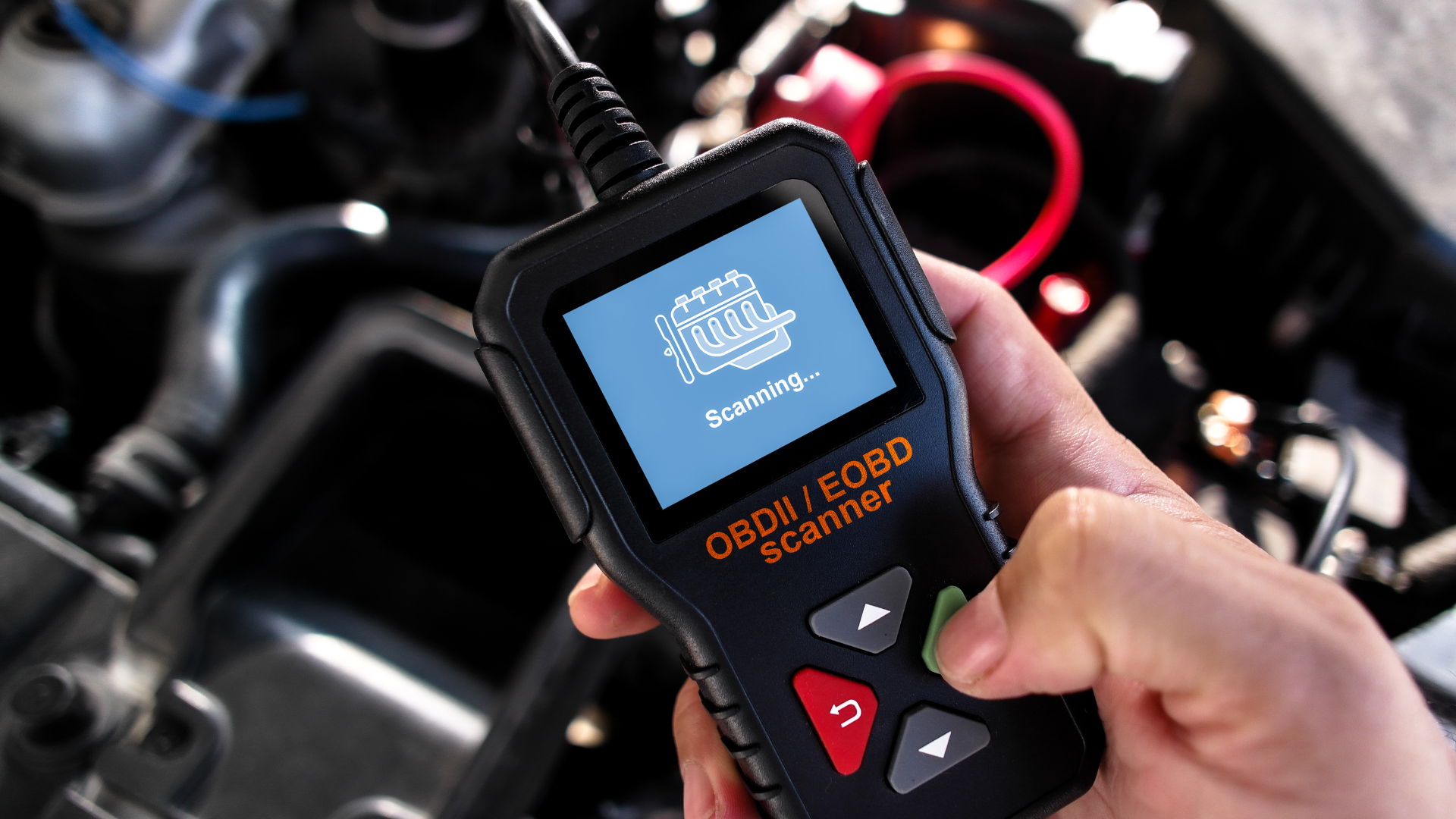 Hand using an OBD2 scanner on a car engine, displaying the check engine light.