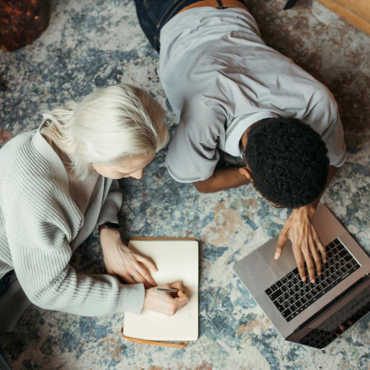 A man and a woman are laying on the floor looking at a laptop