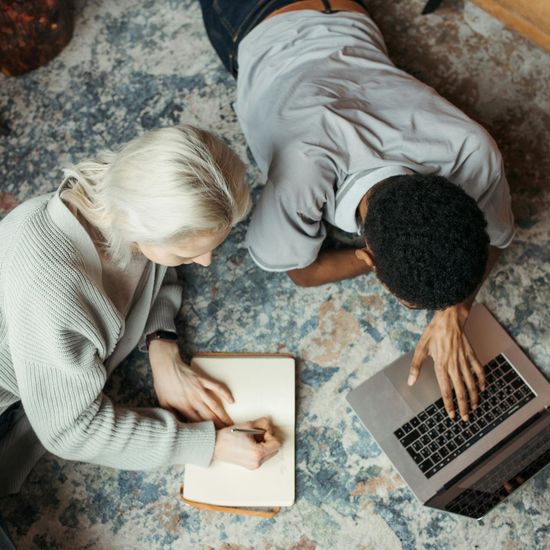 A man and a woman are laying on the floor looking at a laptop