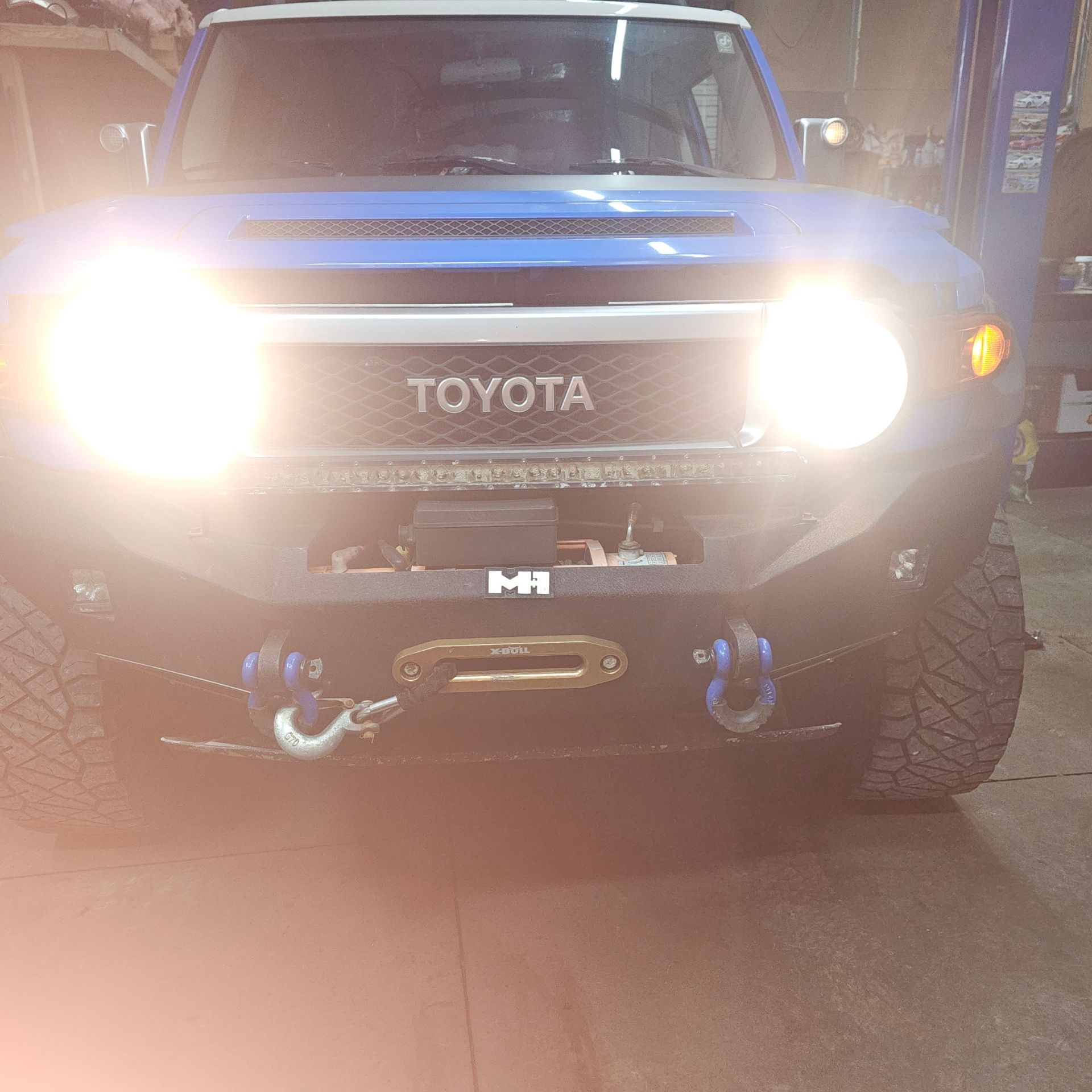 Blue Toyota FJ Cruiser with bright headlights and a custom bumper in a garage.