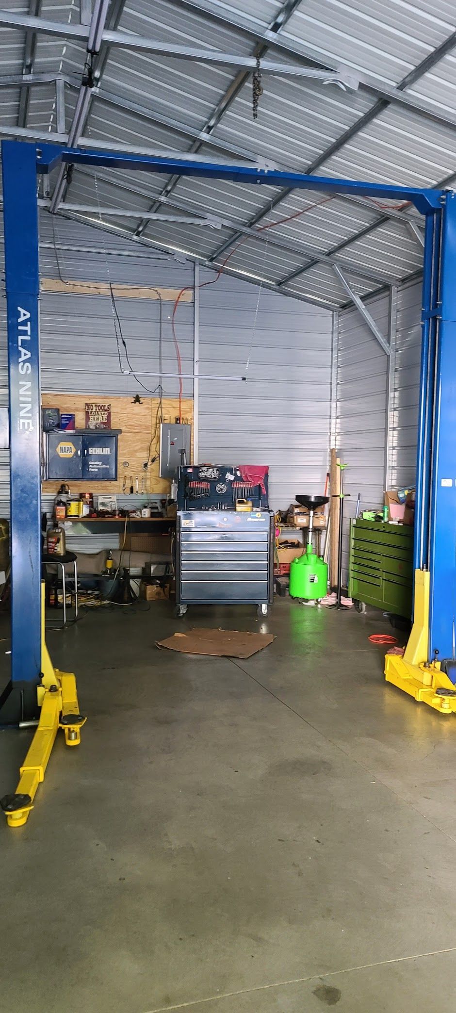Inside a garage with a car lift; tools, shelves, and equipment are visible in the background.