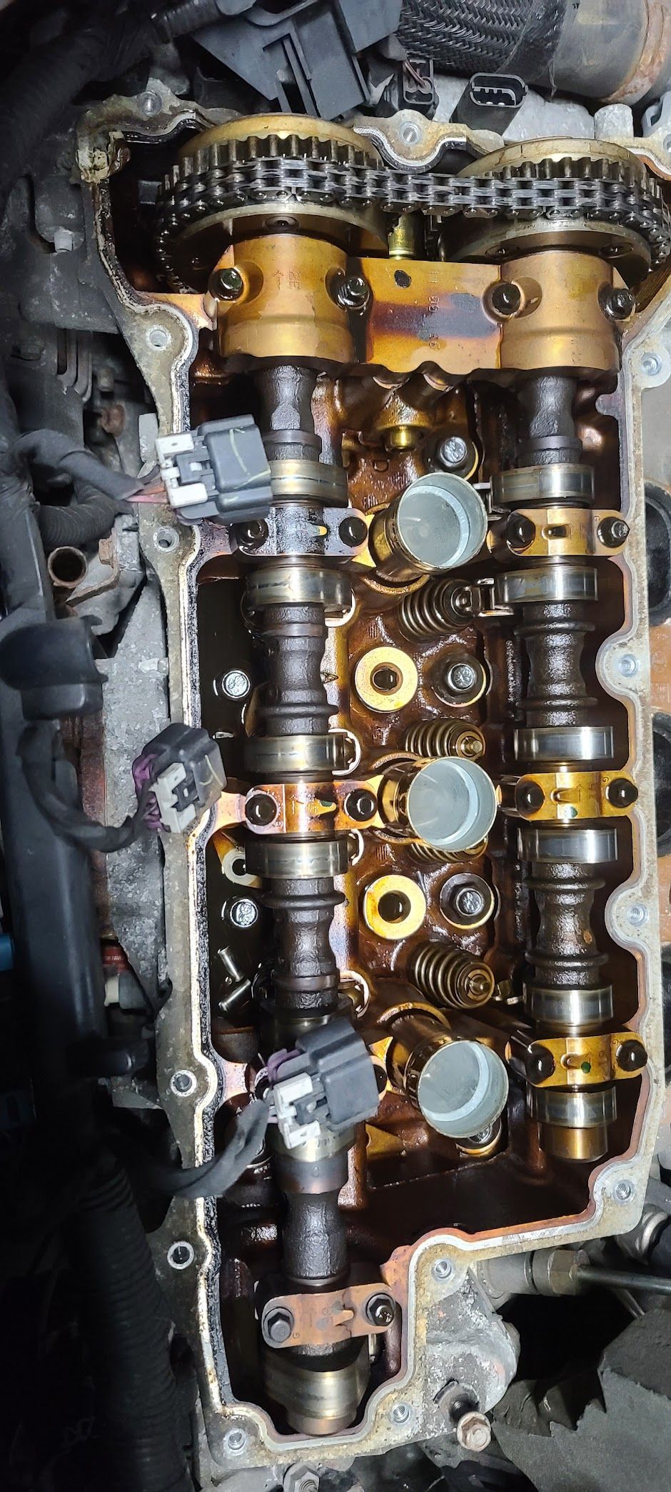 An engine valve train, showing camshafts, chains, and sensors, covered in oil.