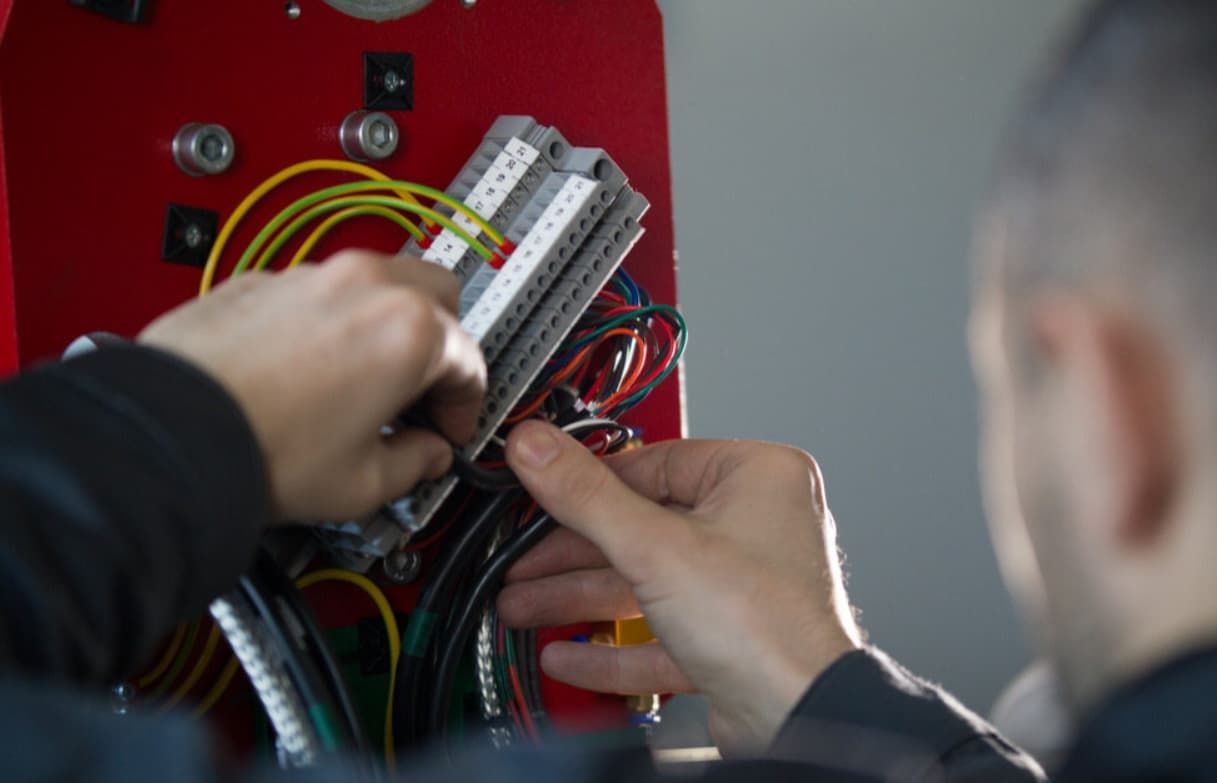 A Man Is Working On A Machine With Wires And A Screwdriver — Mozzlec Electrical In Urangan, QLD