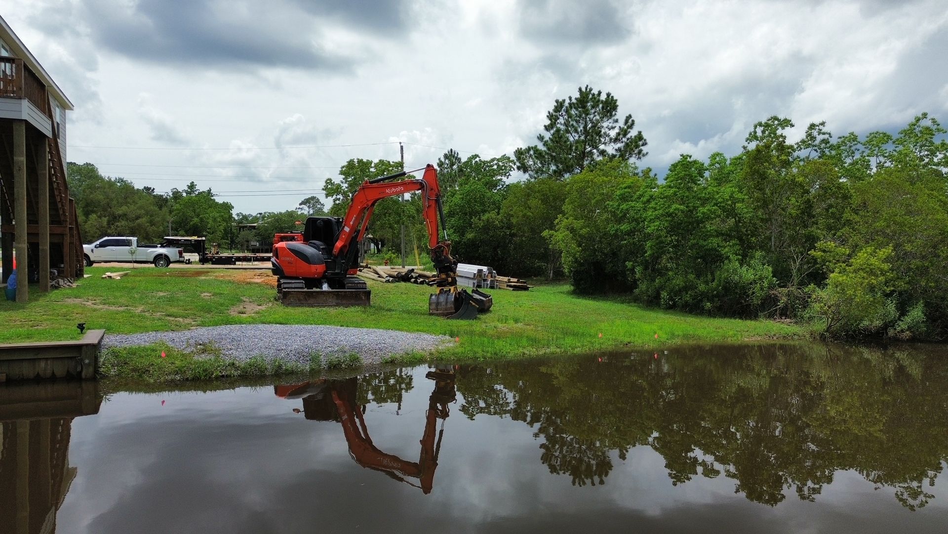 An excavator is sitting in the middle of a flooded field next to a body of water.