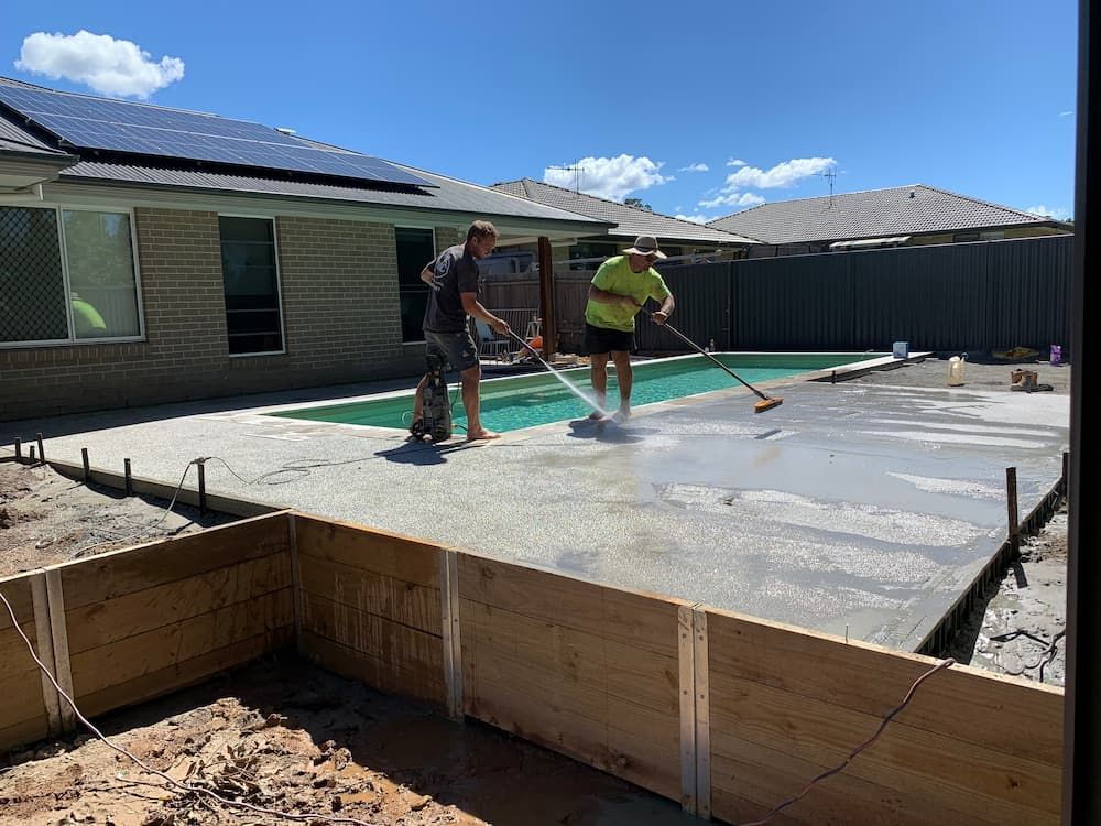 Two Men Are Working On A Concrete Deck In Front Of A Swimming Pool — Brodie Wynter Concreting in Port Macquarie, NSW