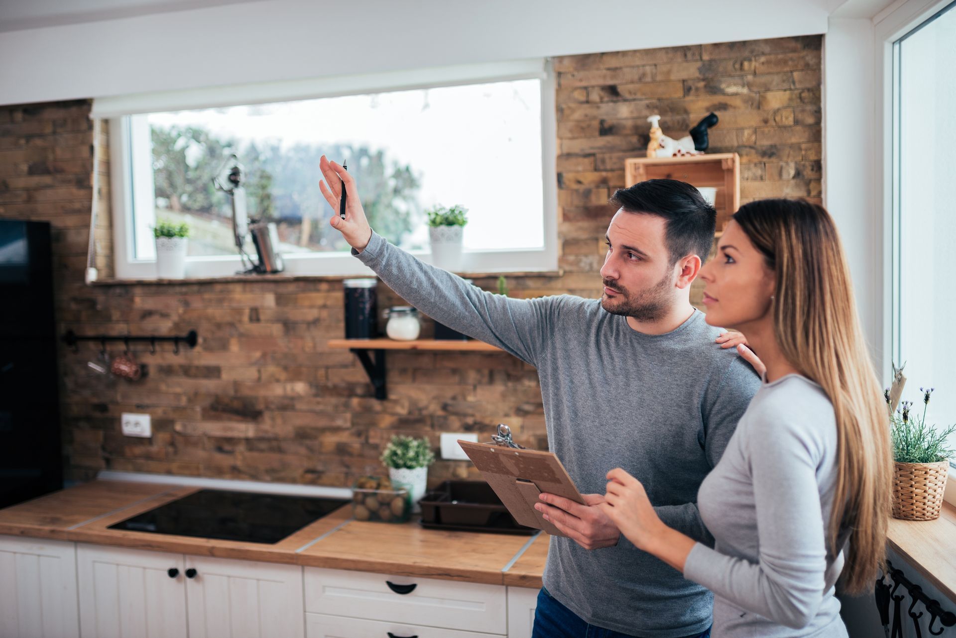 A man and a woman are looking at a clipboard in a kitchen.
