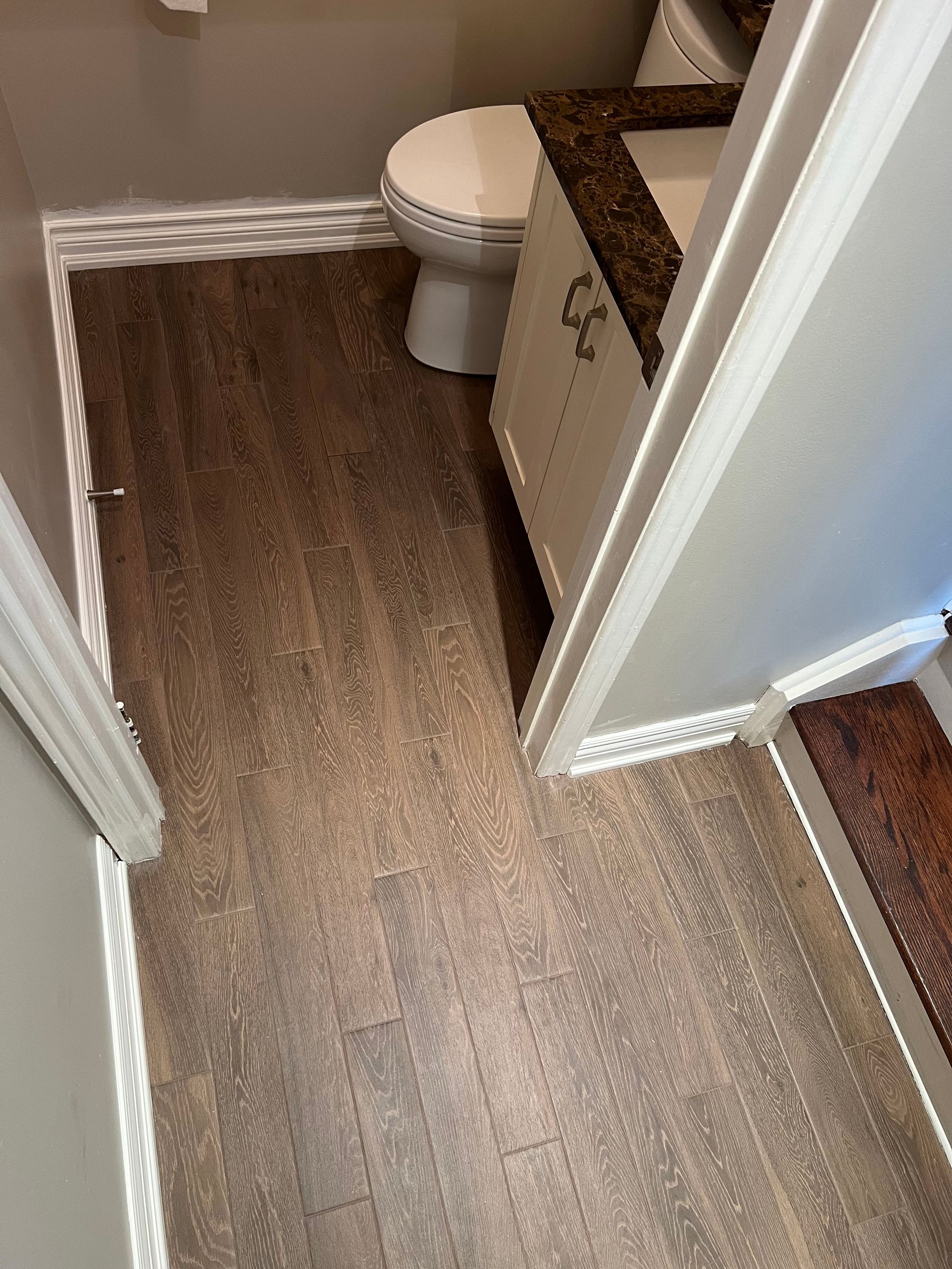 A bathroom with a toilet , sink , and wooden floor.