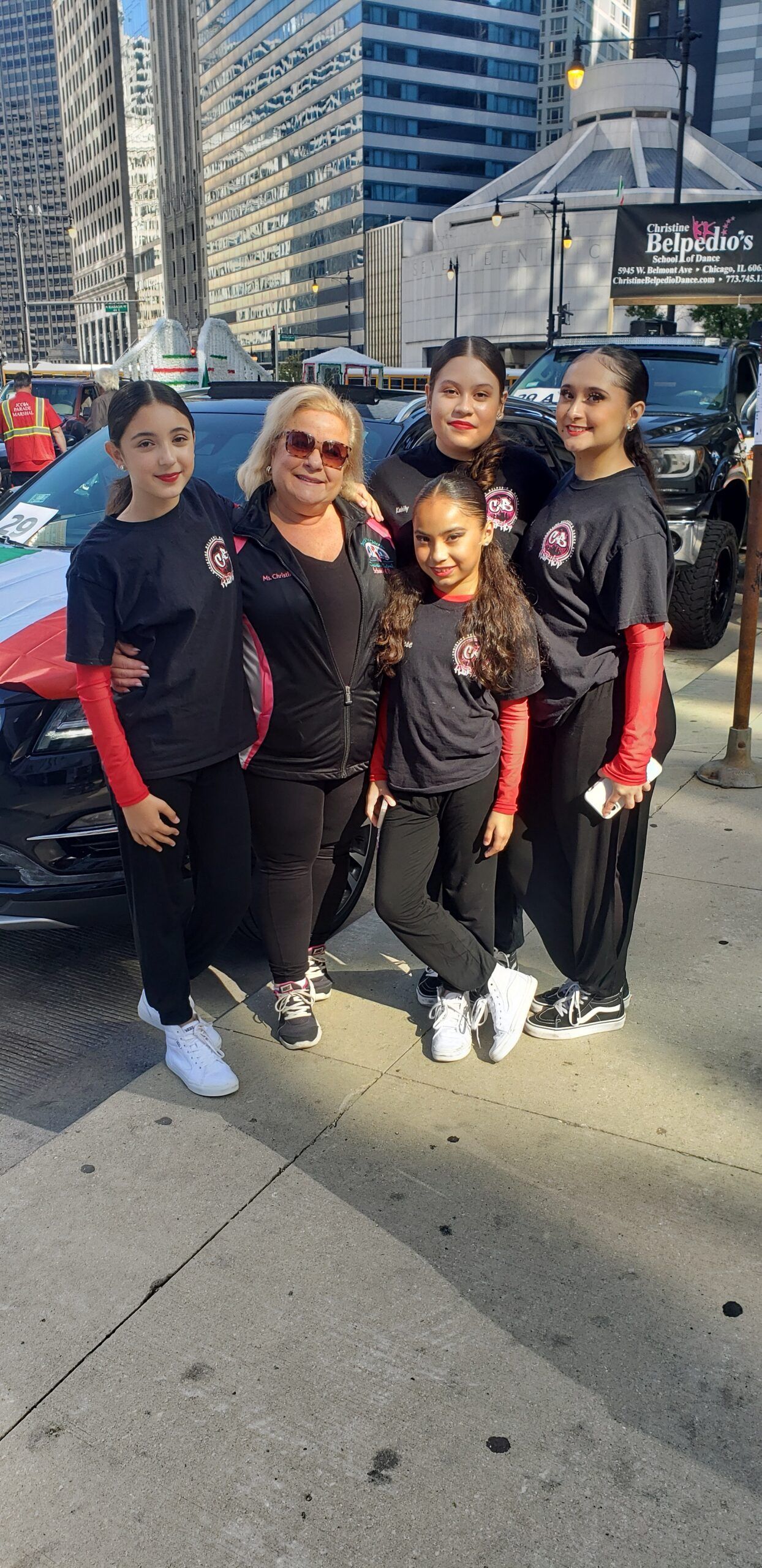 A group of young girls are posing for a picture in front of a car.