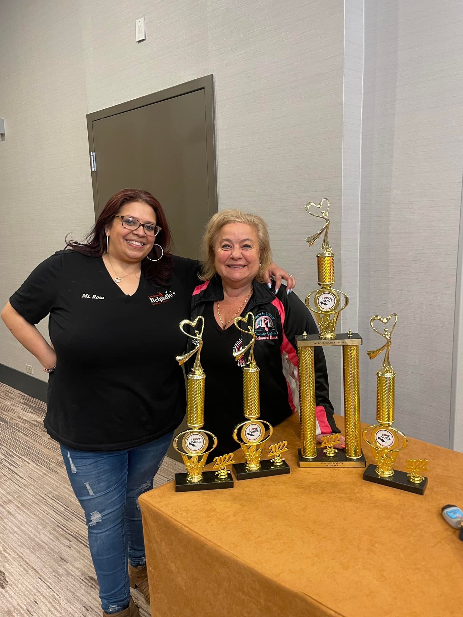 Two women are standing next to a table with trophies on it.
