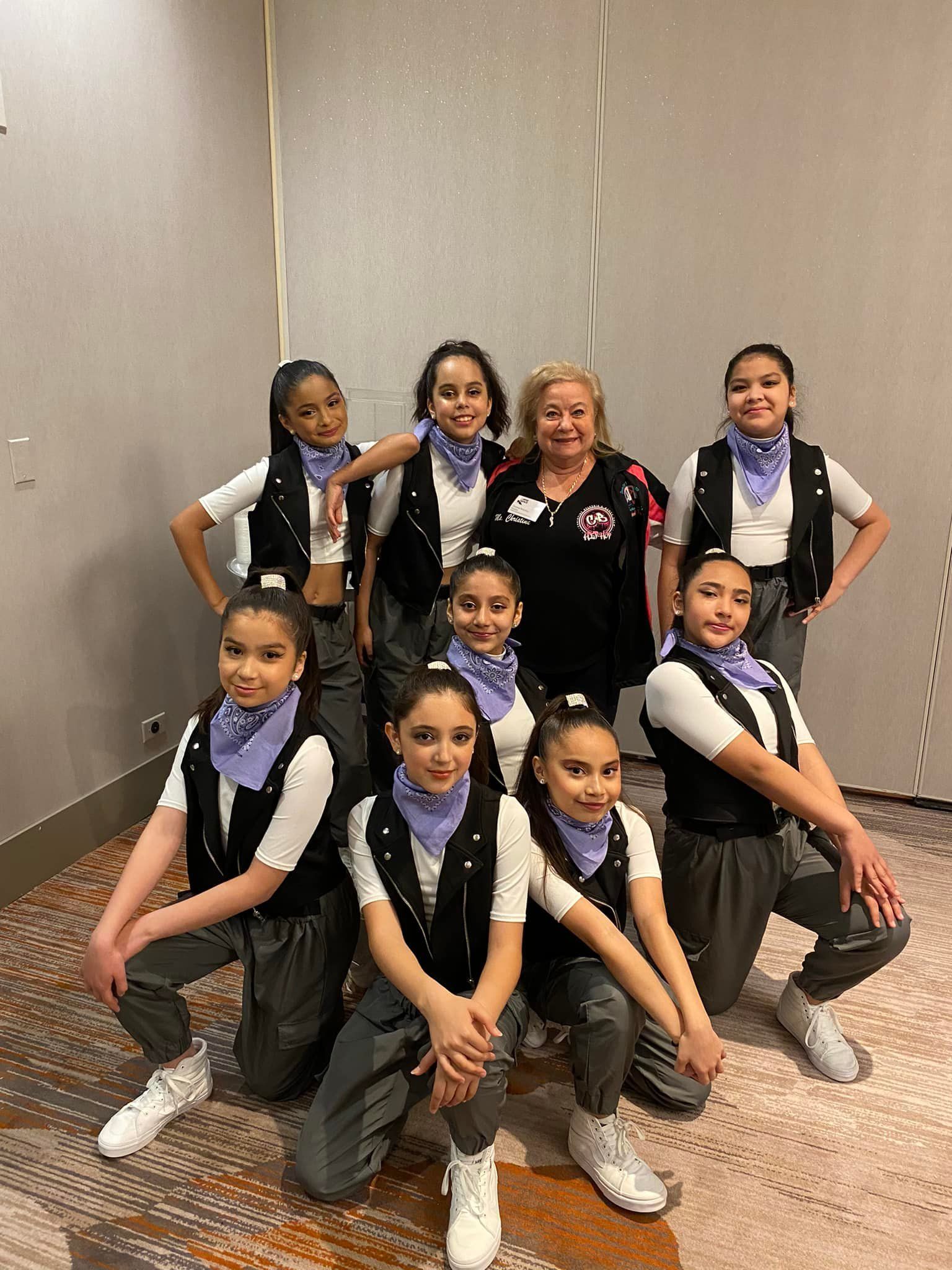 A group of young girls are posing for a picture with a woman in a room.