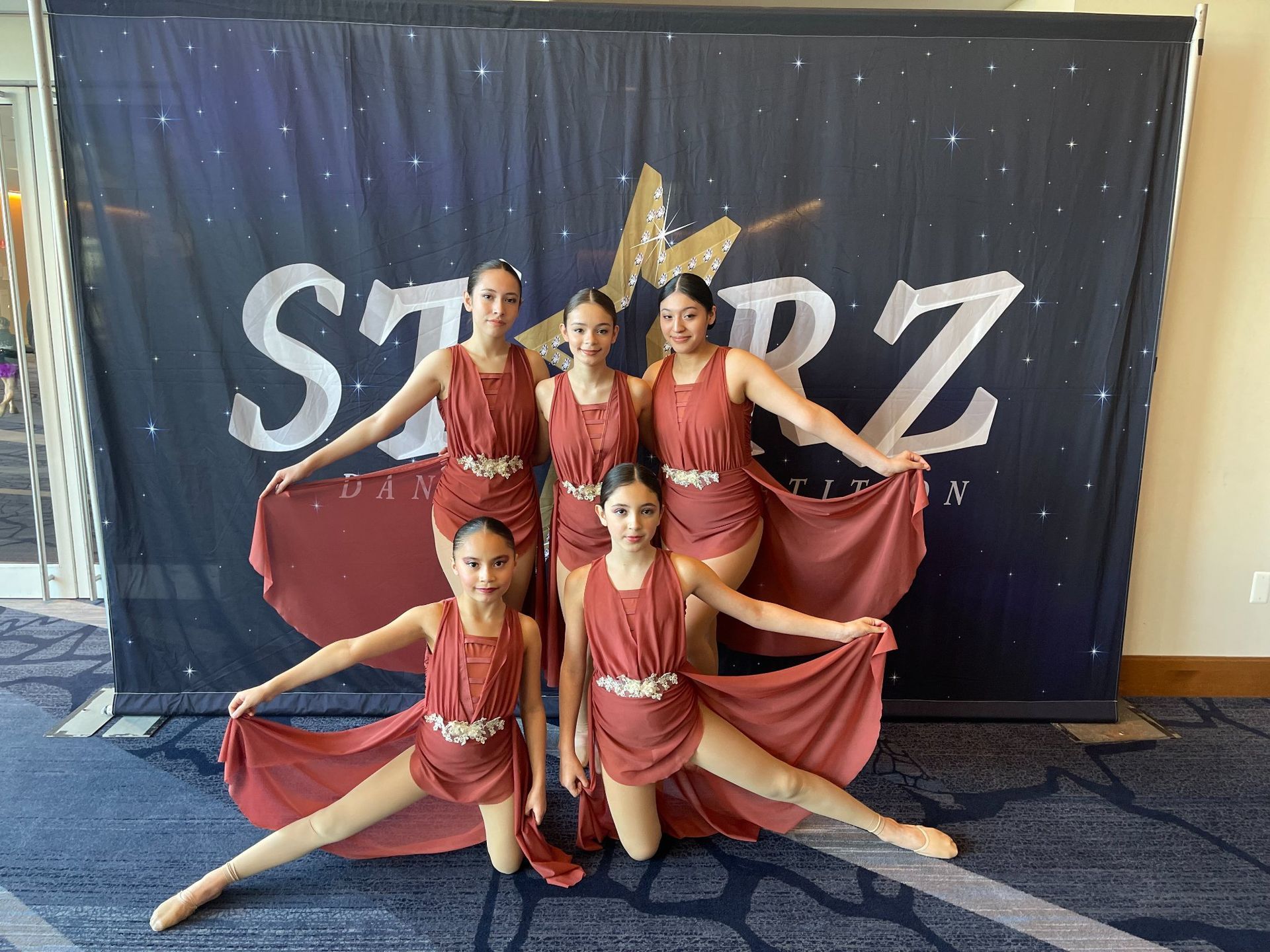 A group of young girls are posing for a picture in front of a starz banner.
