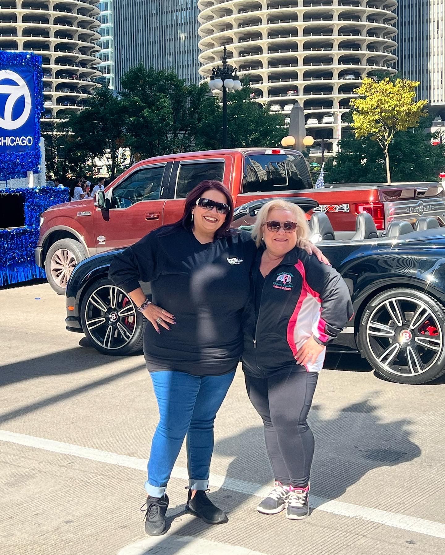 Two women are posing for a picture in front of a truck in a parking lot.